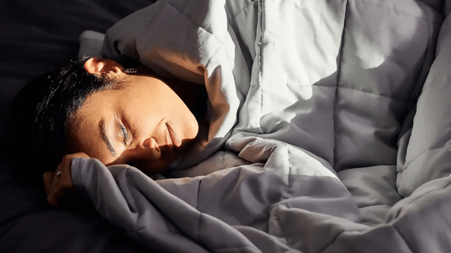 Persoon rust in bed onder een Emma Hug verzwaringsdeken, gezicht zacht verlicht door zonlicht dat door een nabijgelegen raam valt.