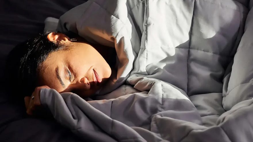 Persoon rust in bed onder een Emma Hug verzwaringsdeken, gezicht zacht verlicht door zonlicht dat door een nabijgelegen raam valt.