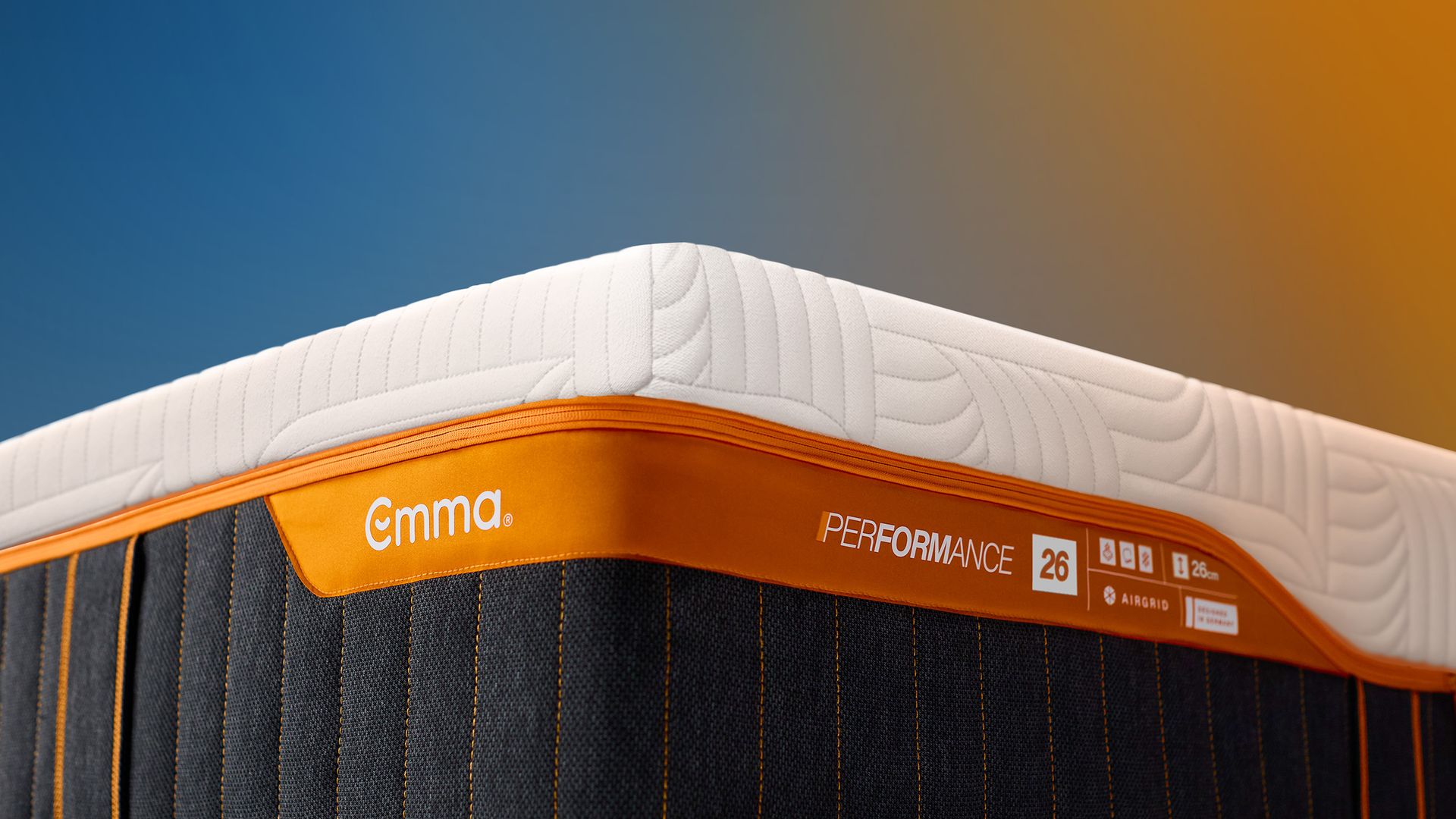 Close-up van een Emma-matras met witte bovenlaag en oranje rand met het label ‘Performance 26’.