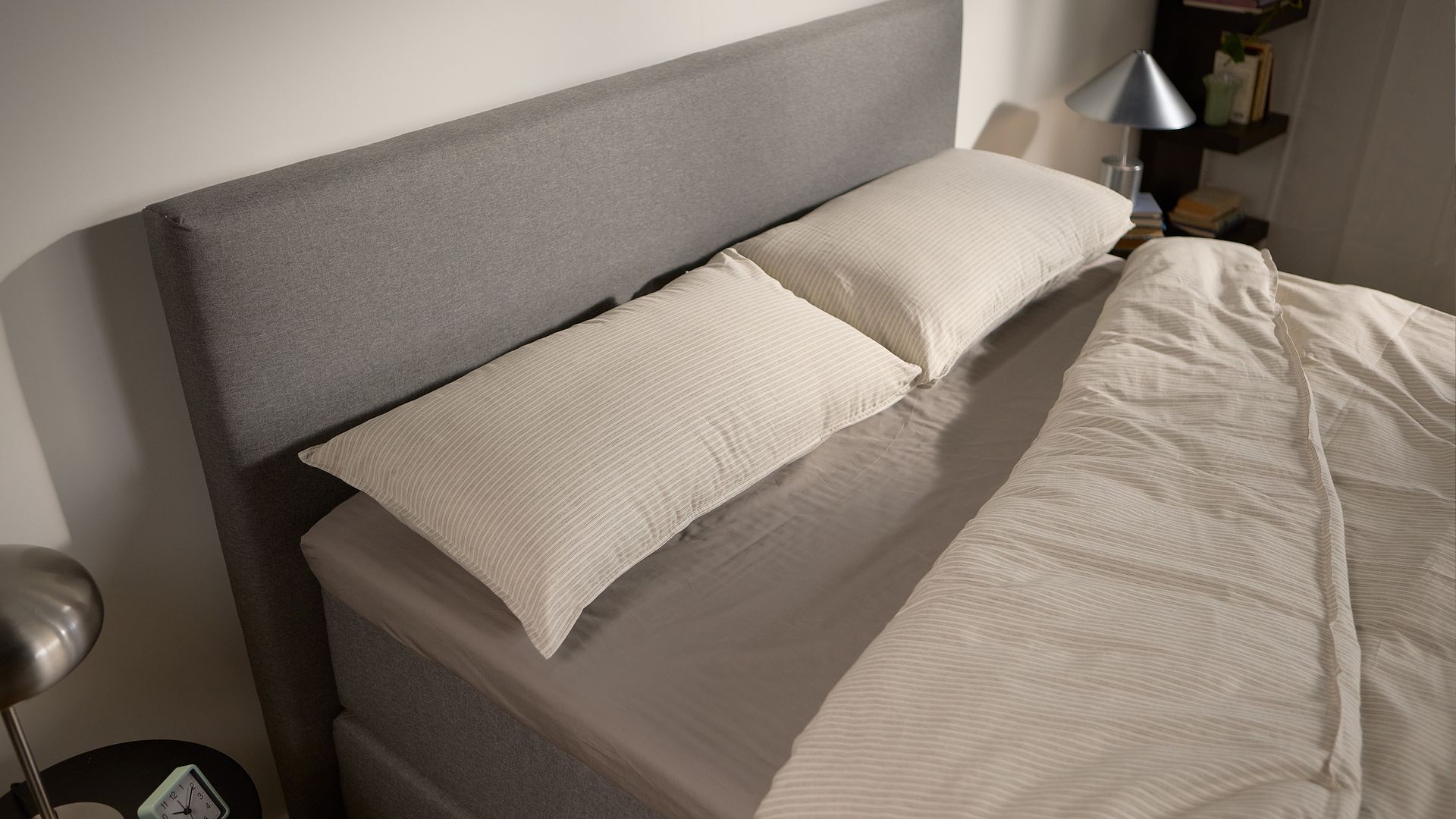 Close-up of the Emma Boxspring Bed in grey showing the upholstered headboard with cream striped pillows.