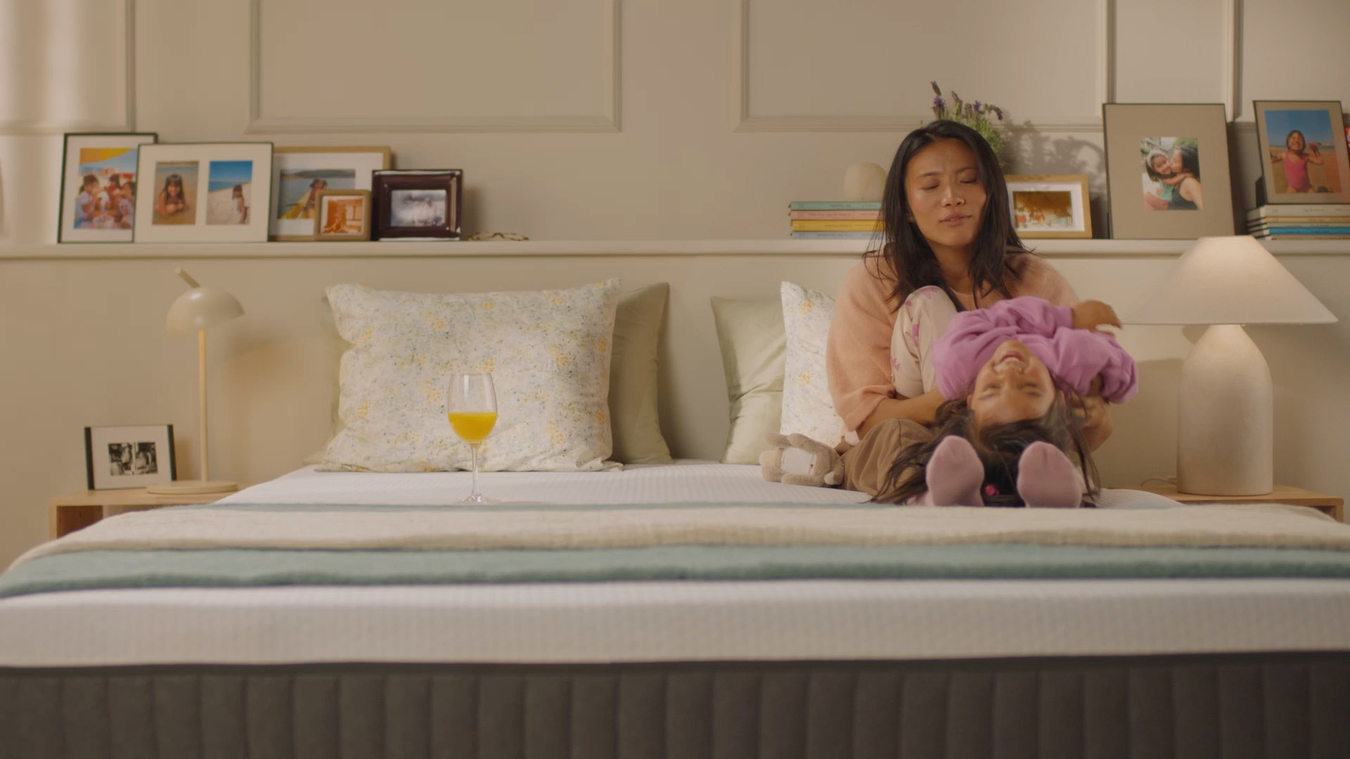 Chambre chaleureuse avec un lit double moderne, où une personne assise joue avec un enfant, mettant en valeur le confort et la stabilité du matelas. Un verre de jus repose sur le lit, illustrant la bonne absorption des mouvements.