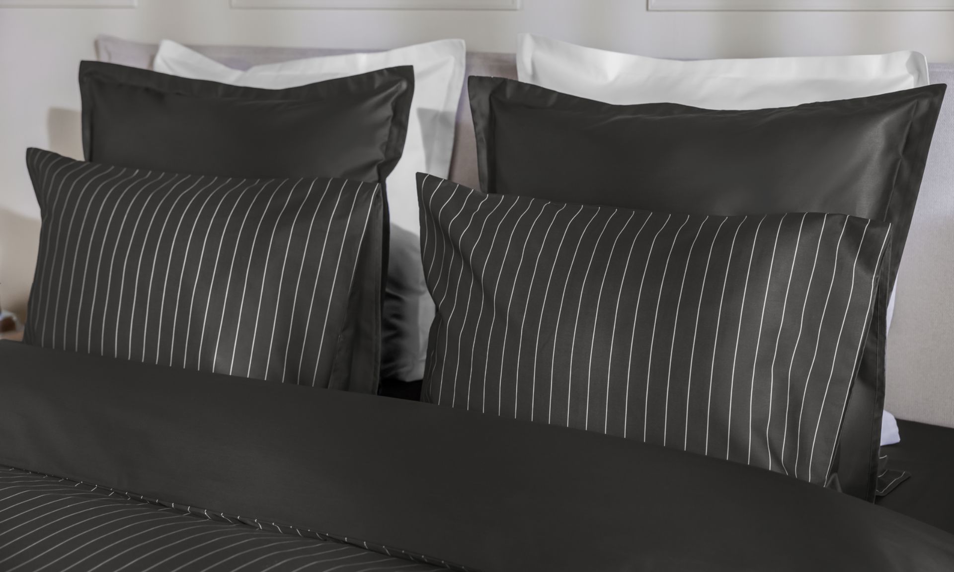 Letto con federe nere a righe bianche, federe nere lisce e due cuscini bianchi.