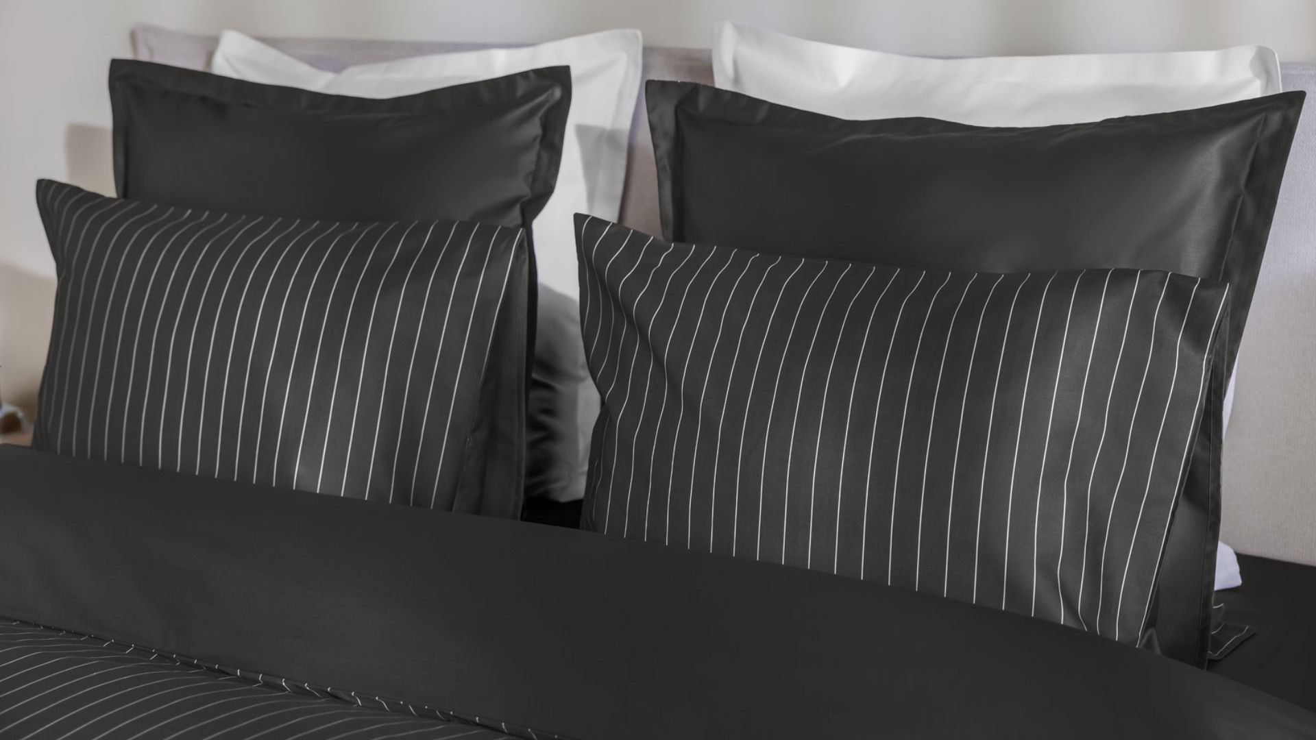 Letto con federe nere a righe bianche, federe nere lisce e due cuscini bianchi.