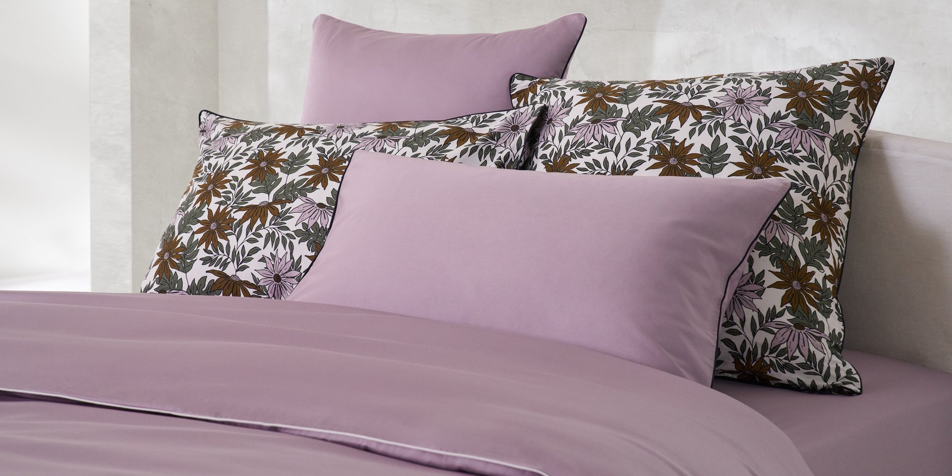 Chambre décorée avec des fleurs, lit gris clair avec une housse de couette florale et des oreillers colorés.