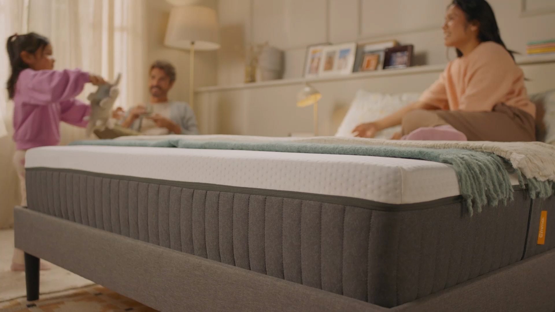 Person sitting on a bed with a white mattress in a bright bedroom.
