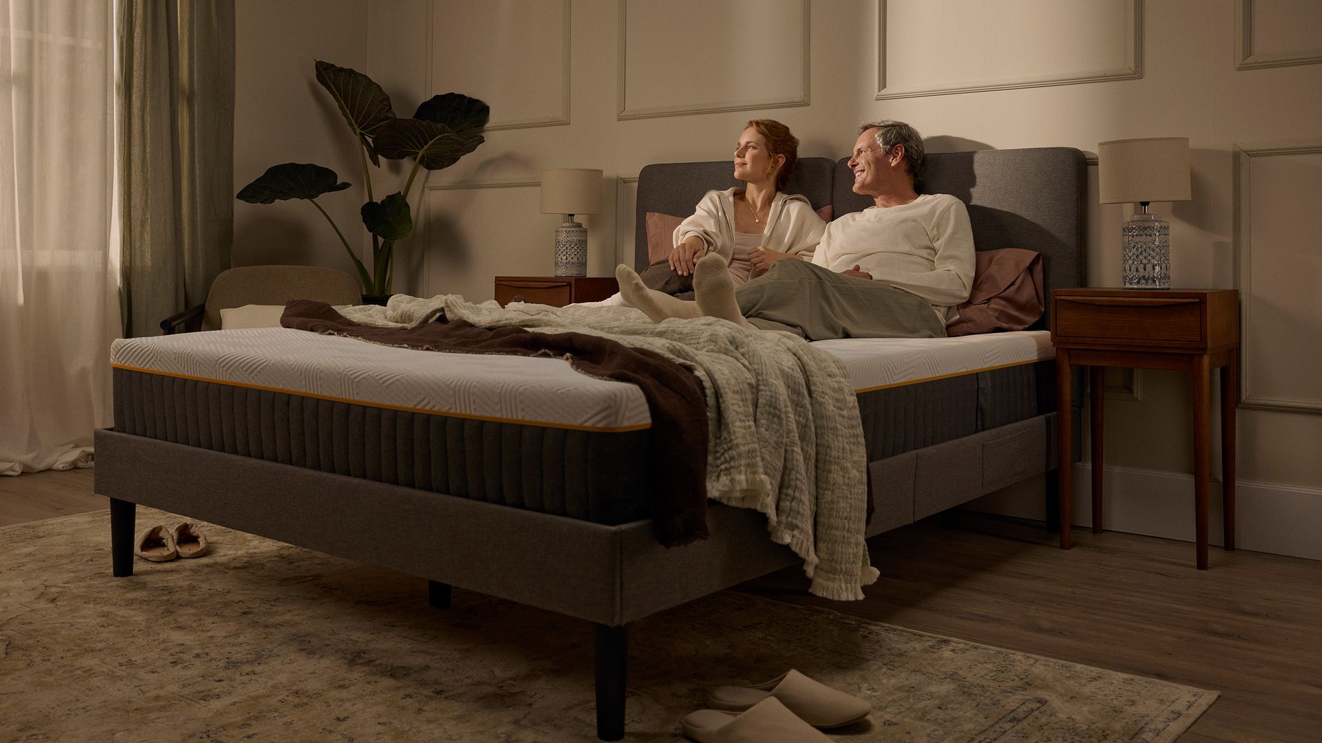 Couple relaxing together on an Emma Original Pro mattress in a warmly lit bedroom.