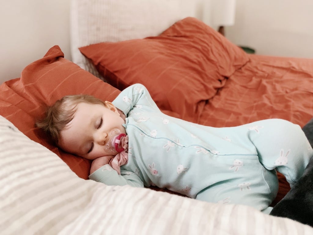 bebe tumbado en una cama durmiendo con las manos en la cara