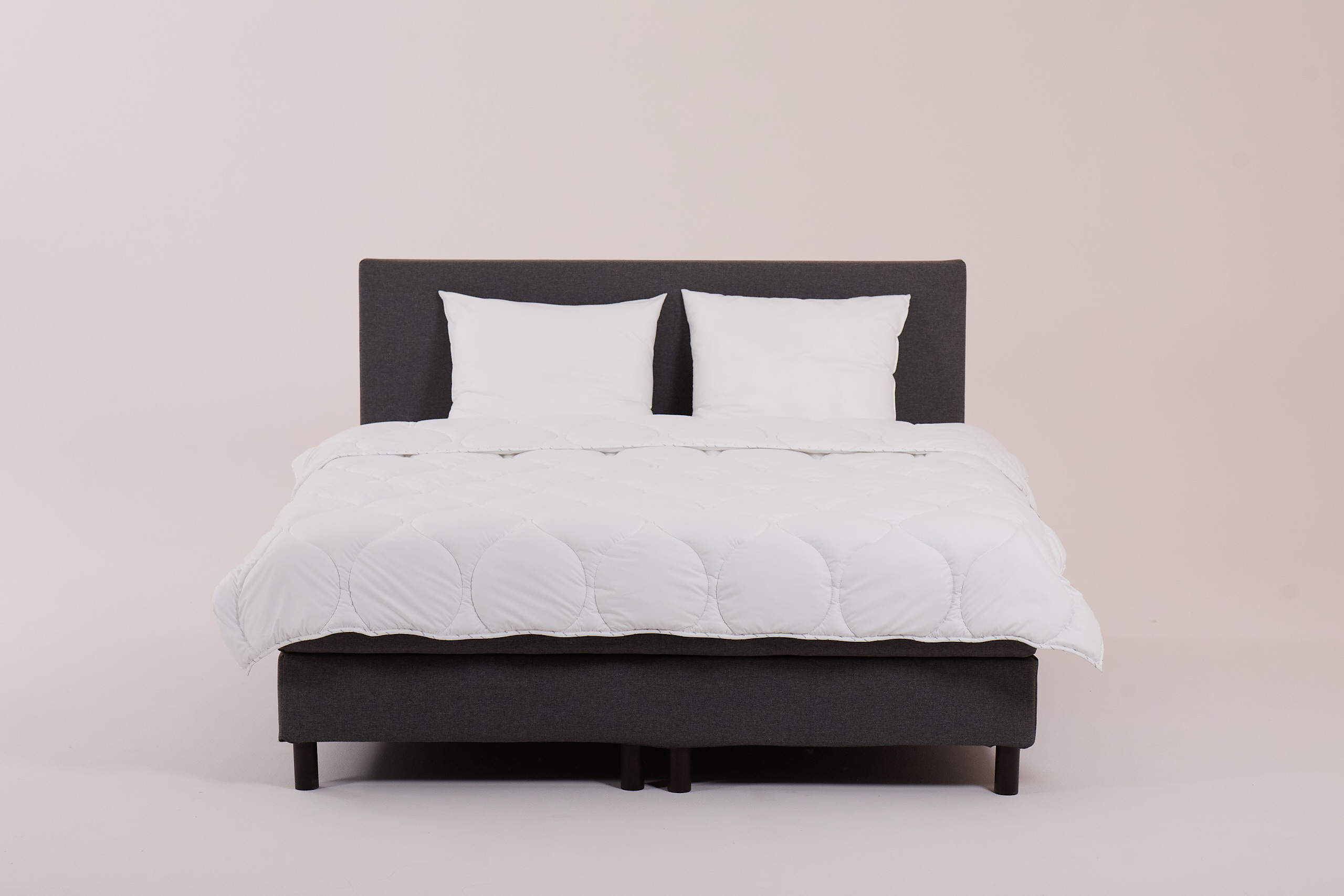 Letto rifatto con testiera e base grigio scuro, piumone e cuscini bianchi.