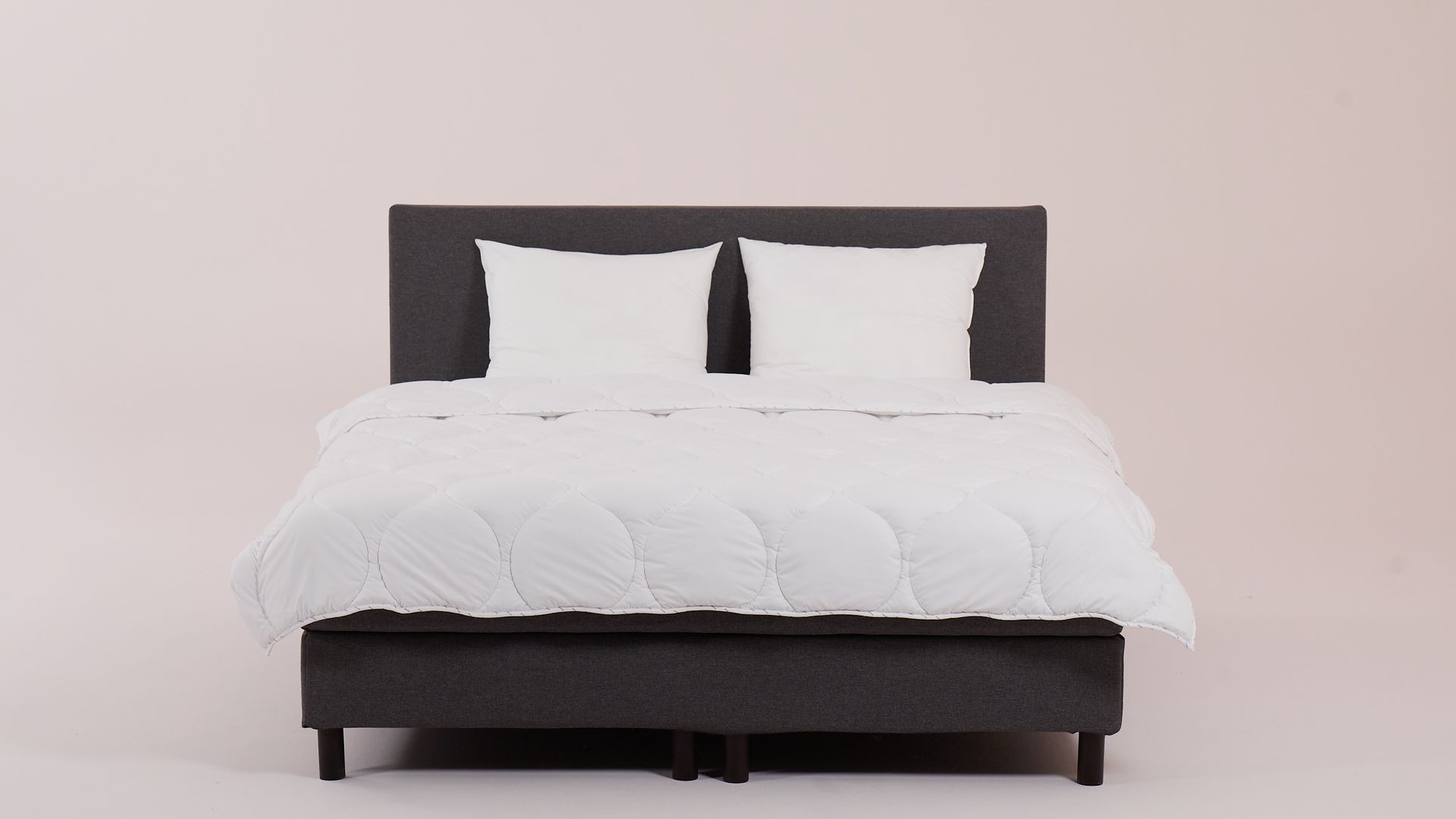 Letto rifatto con testiera e base grigio scuro, piumone e cuscini bianchi.