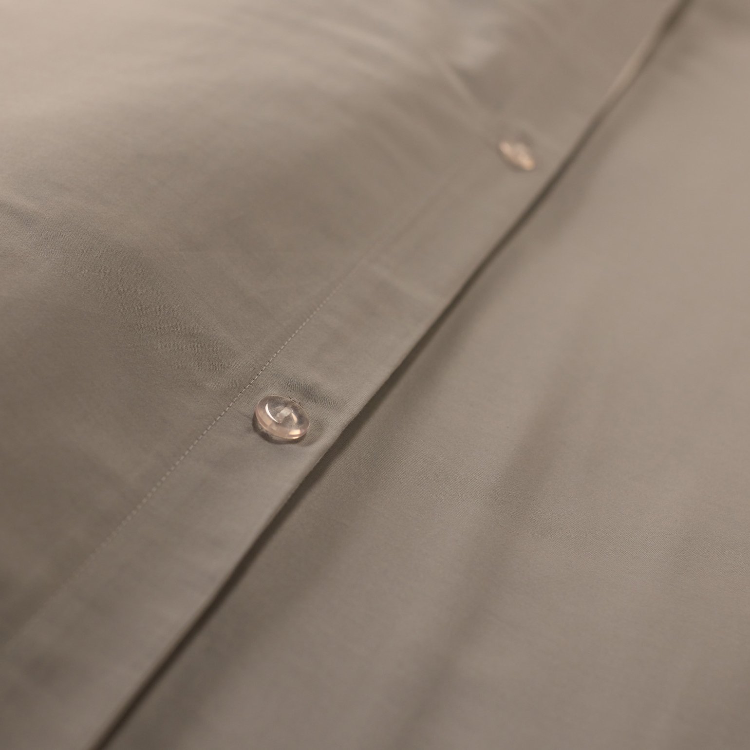 Close‑up van beige beddengoed met een rij knopen op de sluiting.