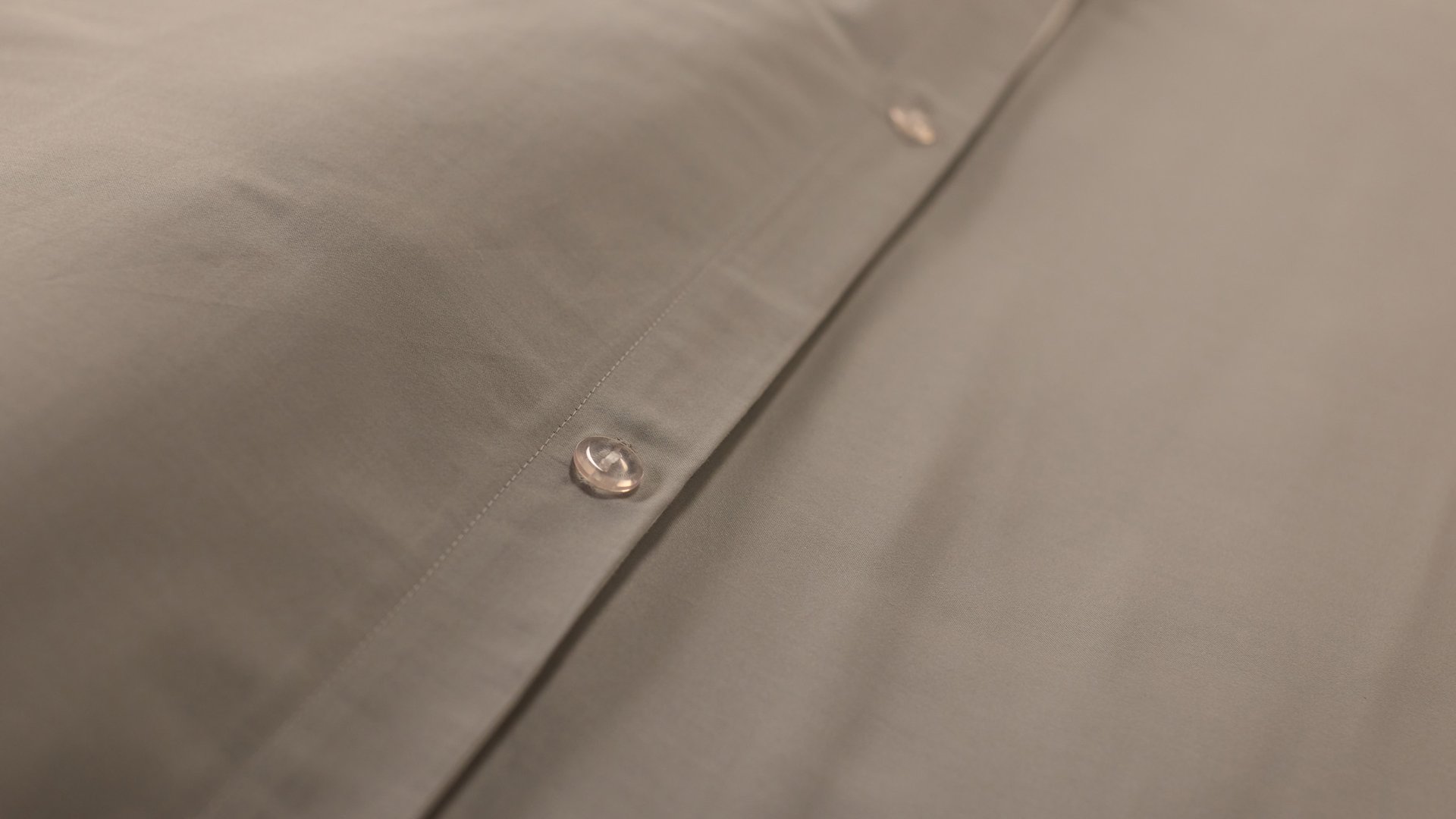 Close‑up van beige beddengoed met een rij knopen op de sluiting.