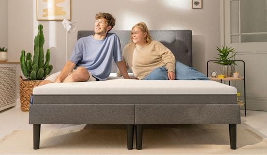 Pareja sonriente sentada en el colchón de espuma viscoelástica y muelles ensacados con tecnología termorreguladora Emma Hybrid Premium+