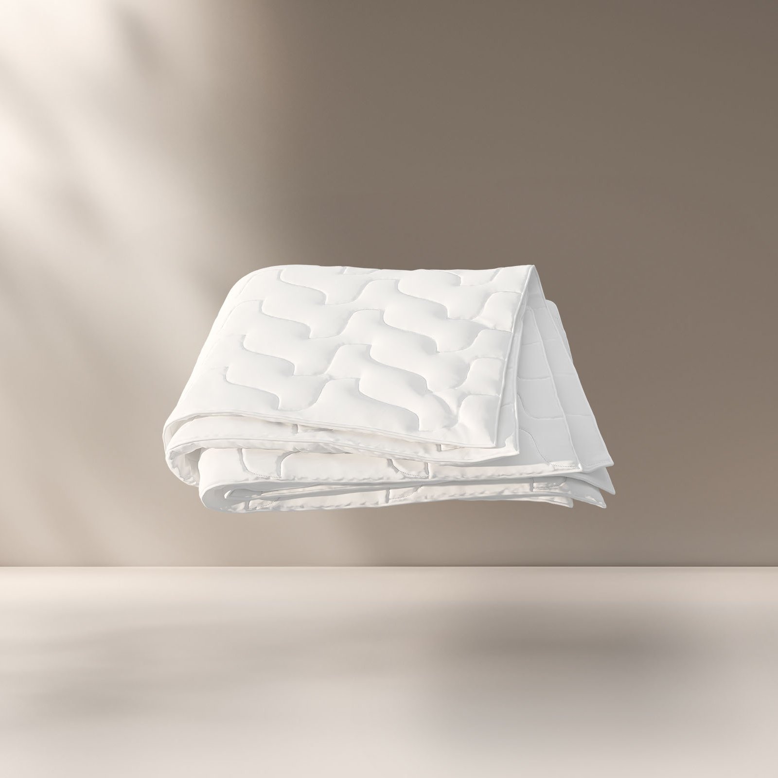 Une couverture blanche matelassée, soigneusement pliée, flotte sur un fond beige doux avec de légers motifs d'ombre et de lumière.