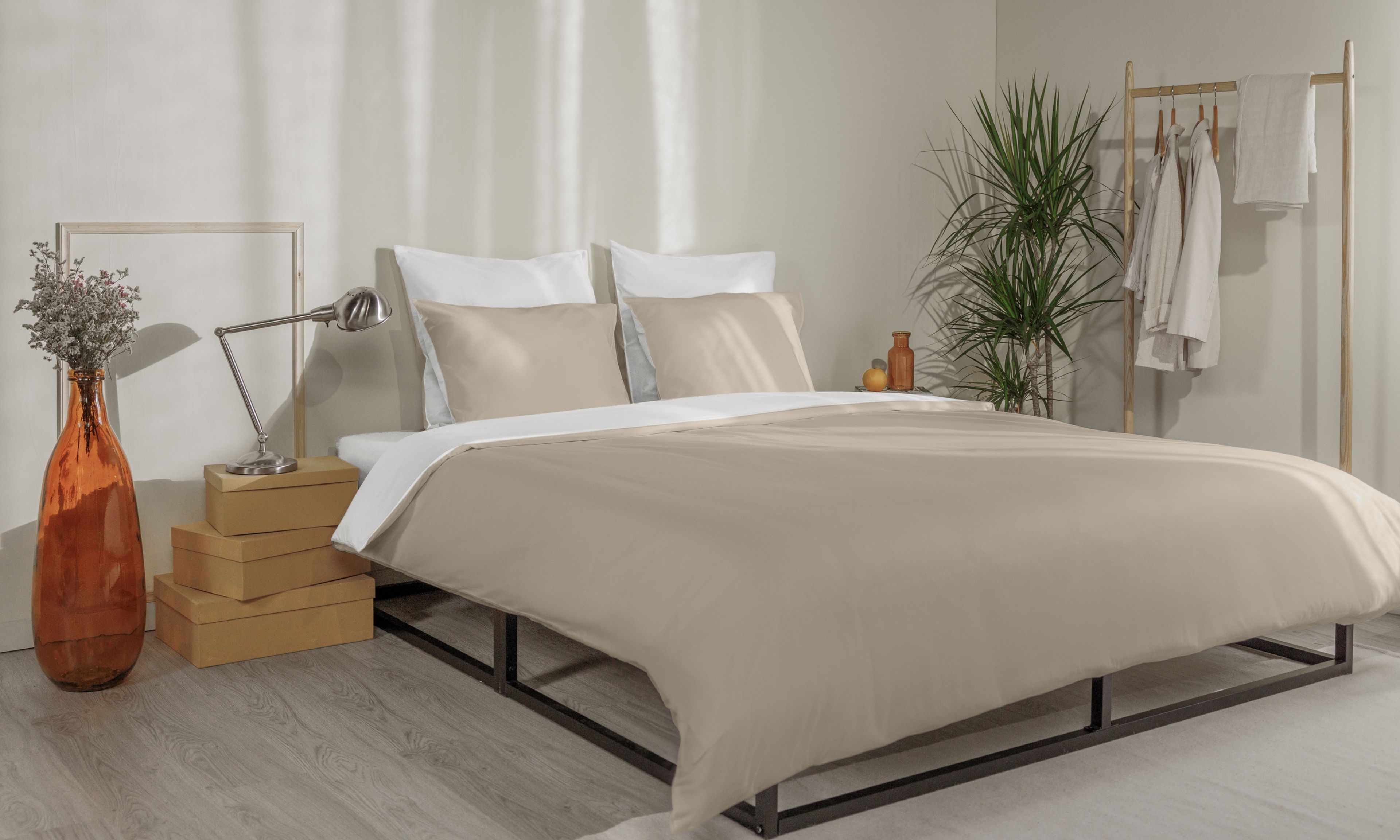 Letto con federe beige e bianche, copripiumino coordinato e testiera in legno a doghe.