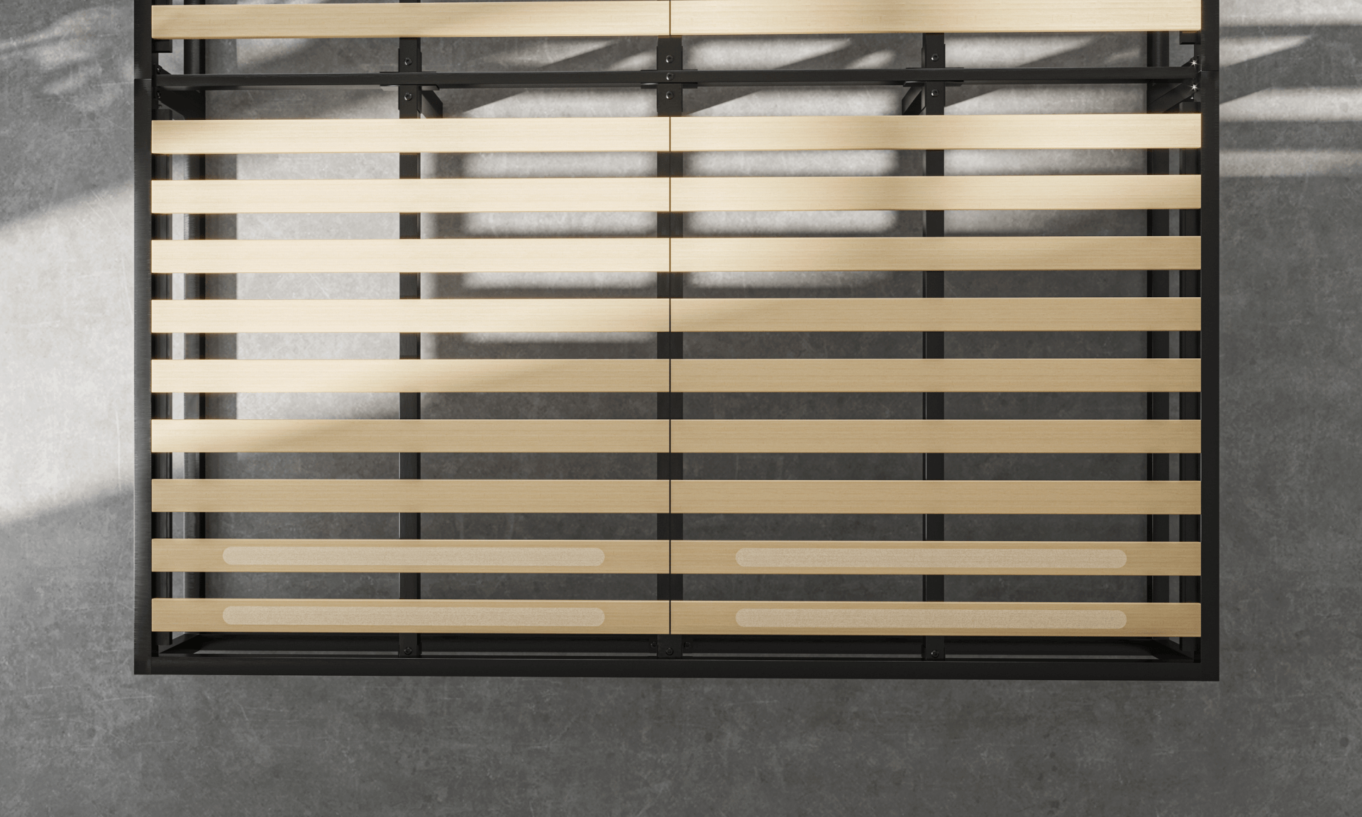 Zwart metalen bedframe met houten lattenbodem, geplaatst op grijze betonnen vloer; latten gelijkmatig verdeeld, twee onderste latten met extra versterkingspatches; lichtinval van links werpt schaduwen op vloer en bedframe.