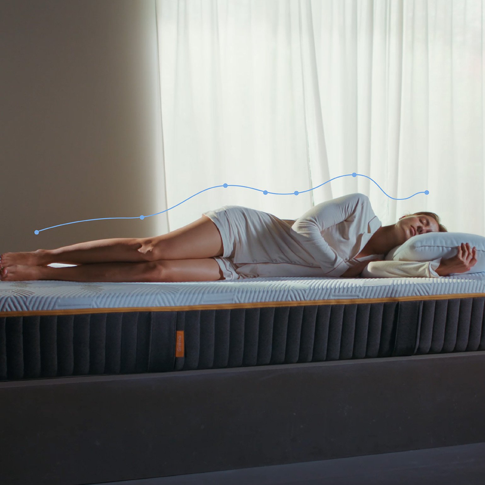 Woman lying on her side on an Emma Original Elite mattress with a spinal alignment graphic overlay showing body support in a bright room.