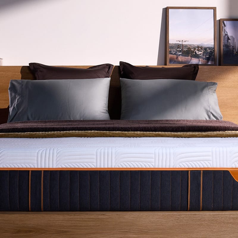 Front view of mattress in a room, showcasing it's height, dark base and white cover, with the orange Emma logo and zipper.