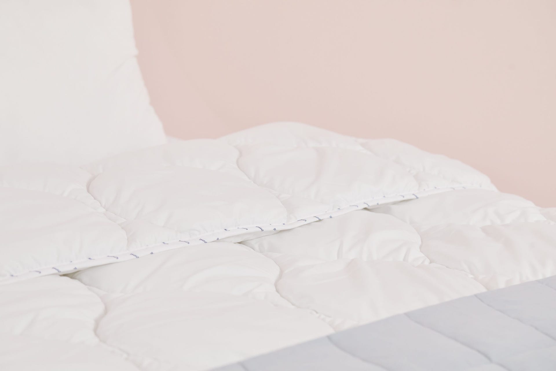 edredón blanco con almohada y fondo rosa