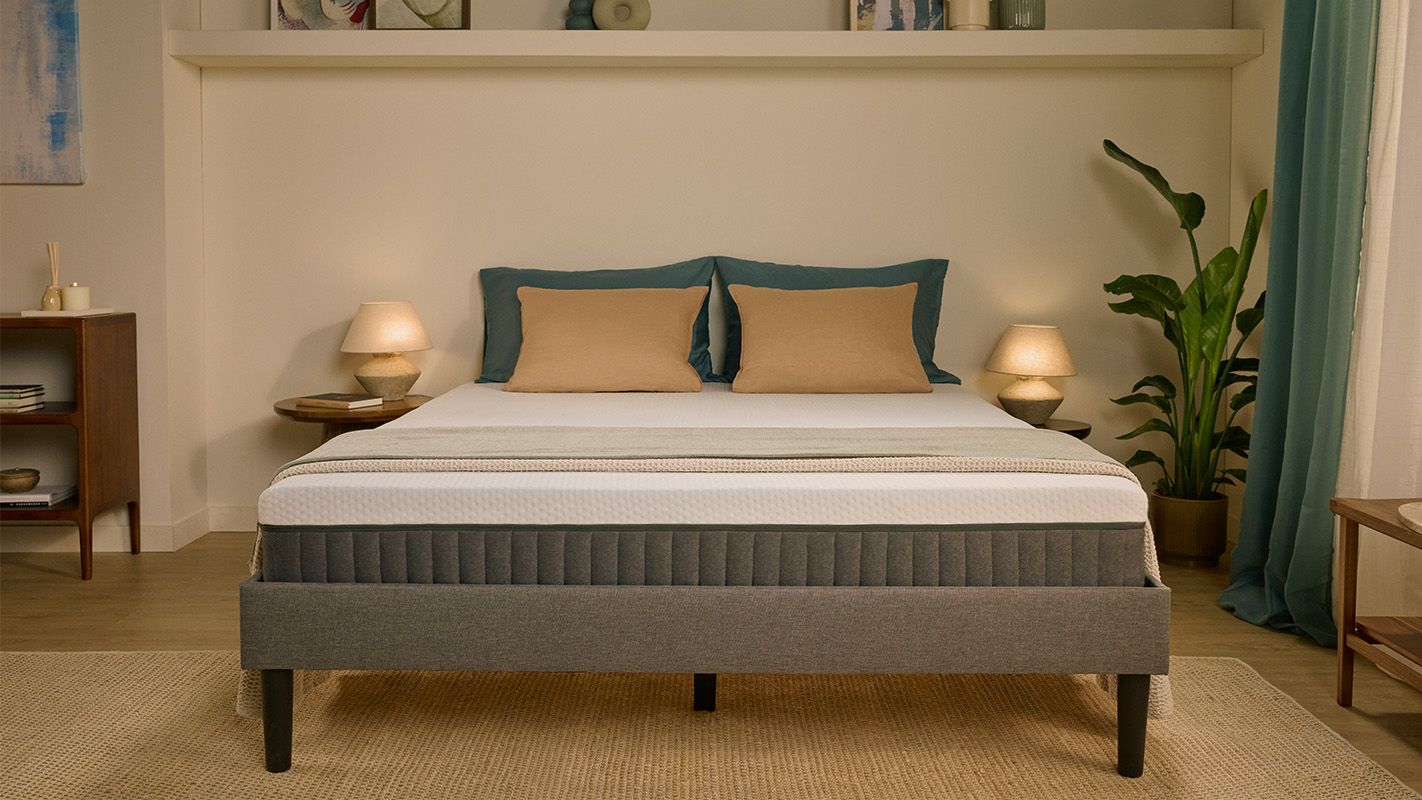 Grijs gestoffeerd bed met wit matras, in een slaapkamer.