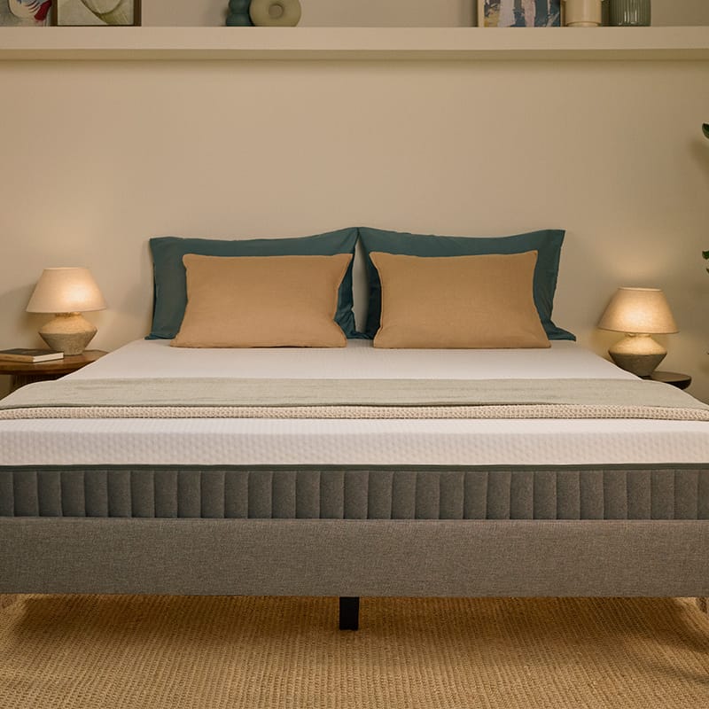 Lit tapissé gris avec matelas blanc, dans une chambre.