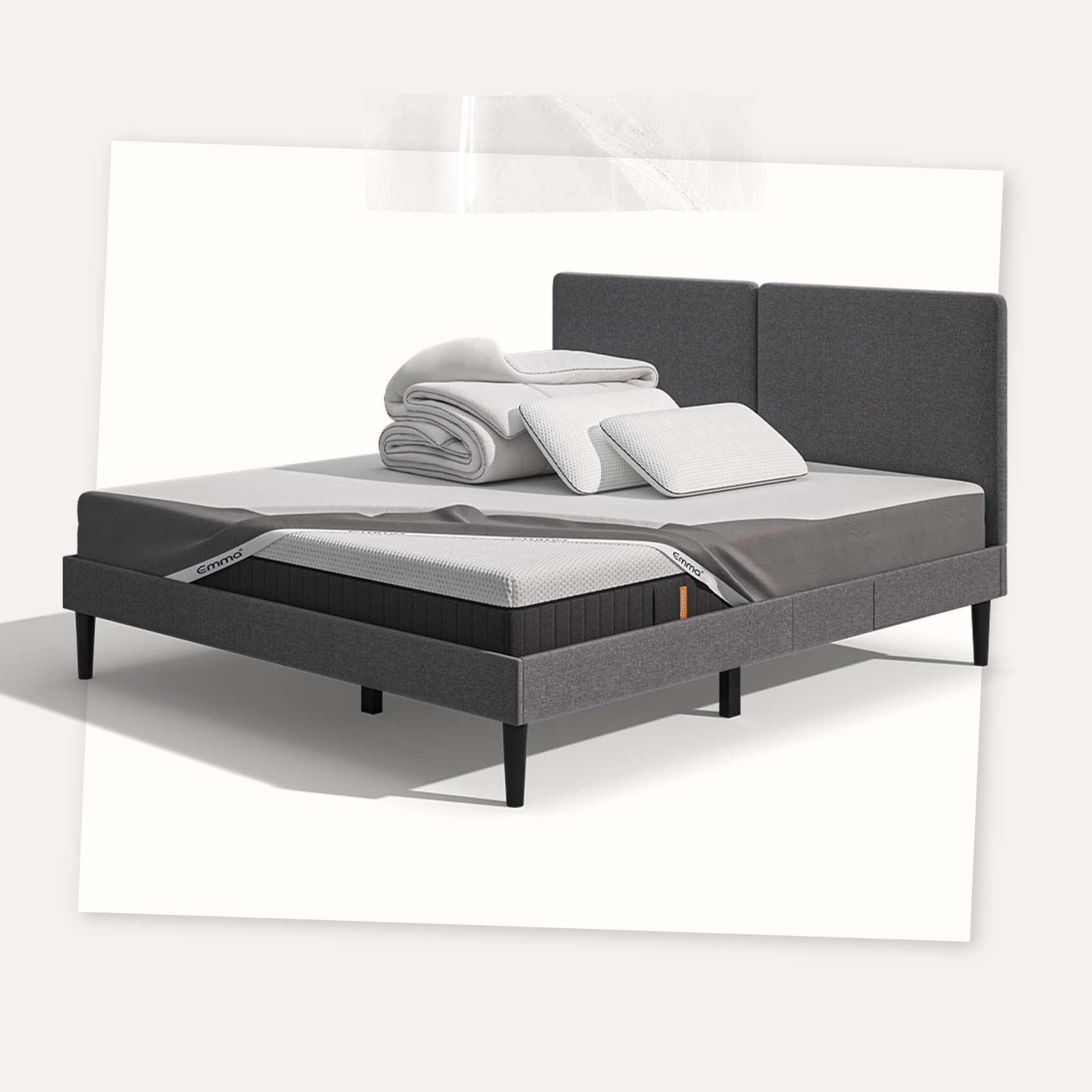 Lit moderne avec tête de lit grise et pieds noirs, recouvert de draps blancs. Deux oreillers blancs et une pile de linge plié sont posés sur le matelas. Arrière-plan beige avec une forme orange abstraite.