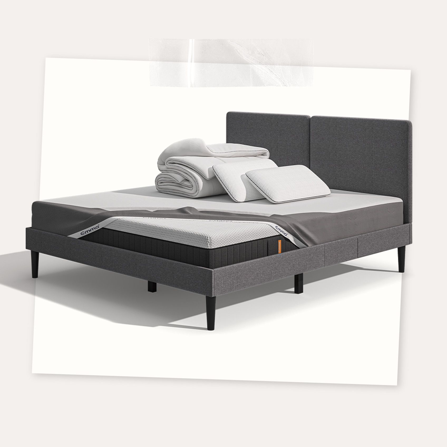 Lit moderne avec tête de lit grise et pieds noirs, recouvert de draps blancs. Deux oreillers blancs et une pile de linge plié sont posés sur le matelas. Arrière-plan beige avec une forme orange abstraite.