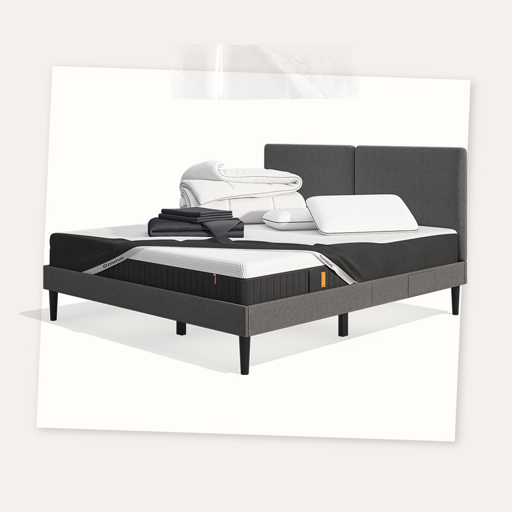 Lit moderne avec tête de lit grise et pieds noirs, recouvert de draps blancs. Deux oreillers blancs et une pile de linge plié sont posés sur le matelas. Arrière-plan beige avec une forme orange abstraite.