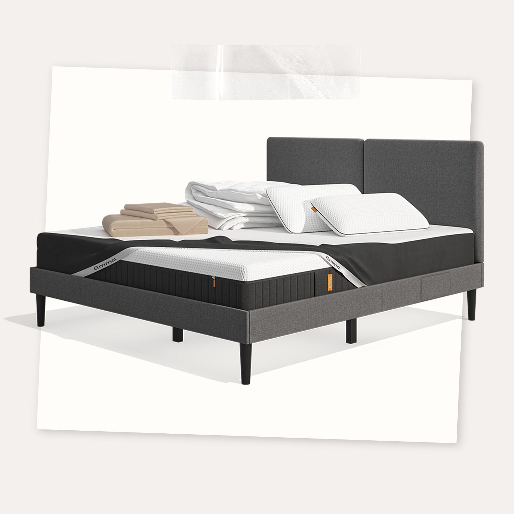 Lit moderne avec tête de lit grise et pieds noirs, recouvert de draps blancs. Deux oreillers blancs et une pile de linge plié sont posés sur le matelas. Arrière-plan beige avec une forme orange abstraite.