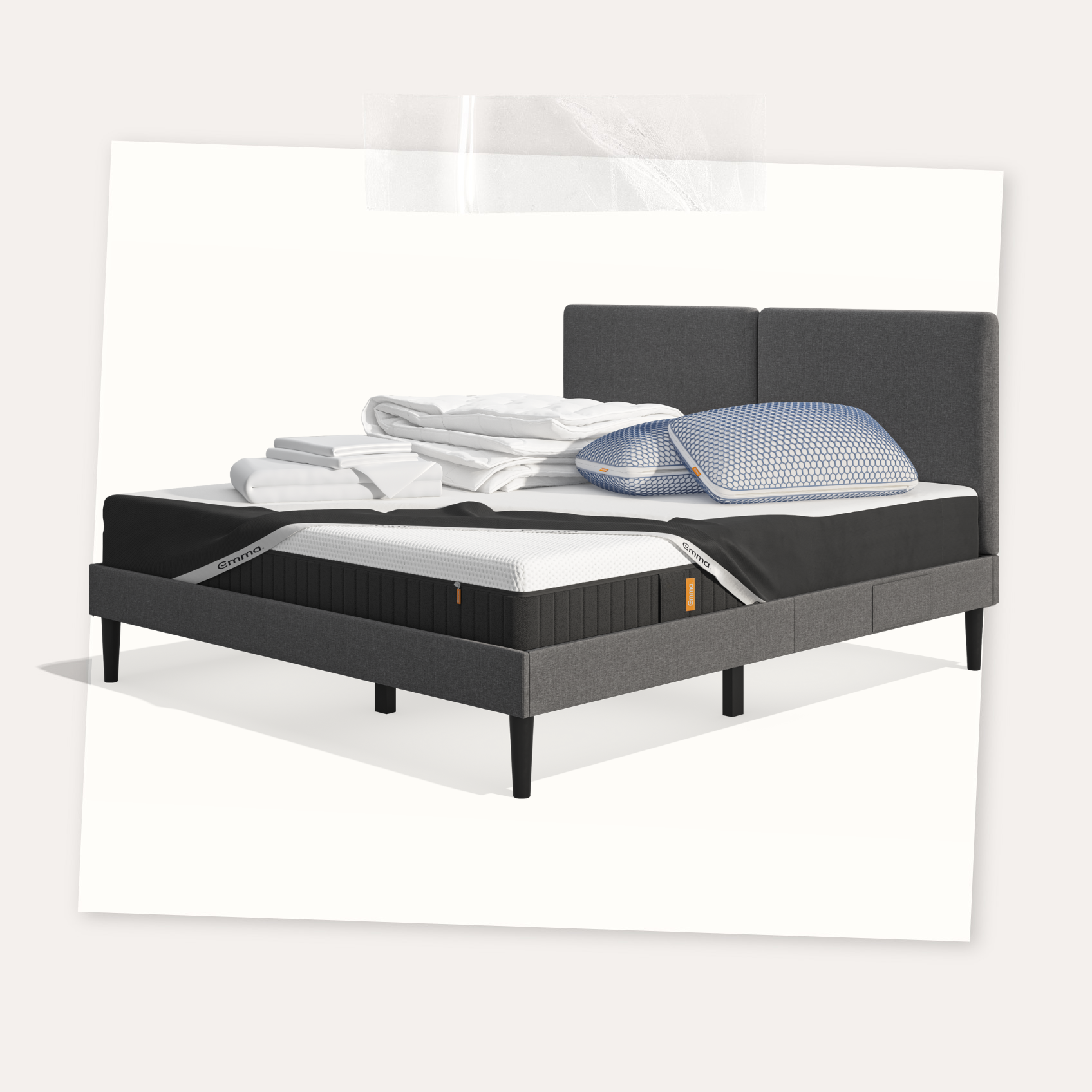 Lit moderne avec tête de lit grise et pieds noirs, recouvert de draps blancs. Deux oreillers blancs et une pile de linge plié sont posés sur le matelas. Arrière-plan beige avec une forme orange abstraite.