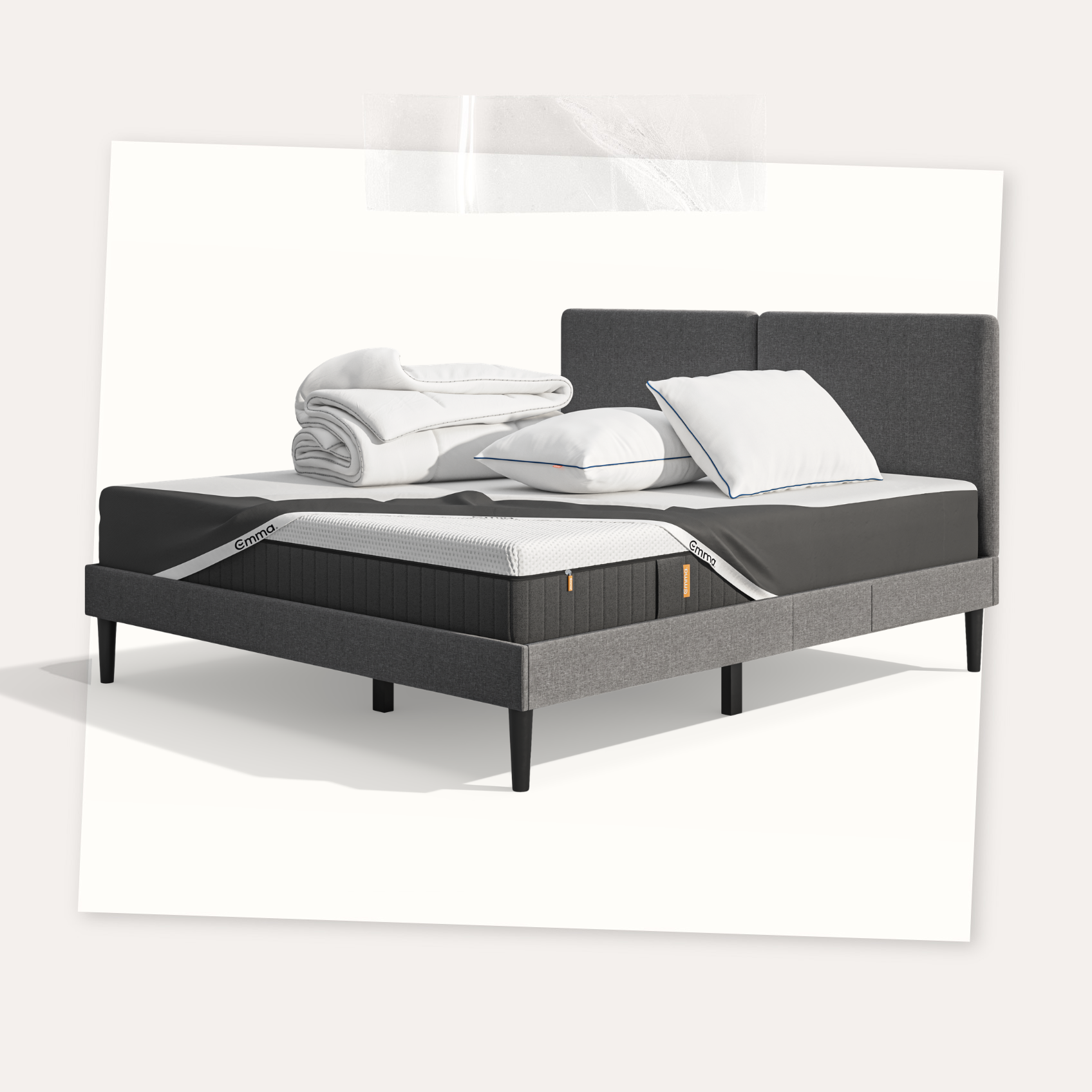 Lit moderne avec tête de lit grise et pieds noirs, recouvert de draps blancs. Deux oreillers blancs et une pile de linge plié sont posés sur le matelas. Arrière-plan beige avec une forme orange abstraite.