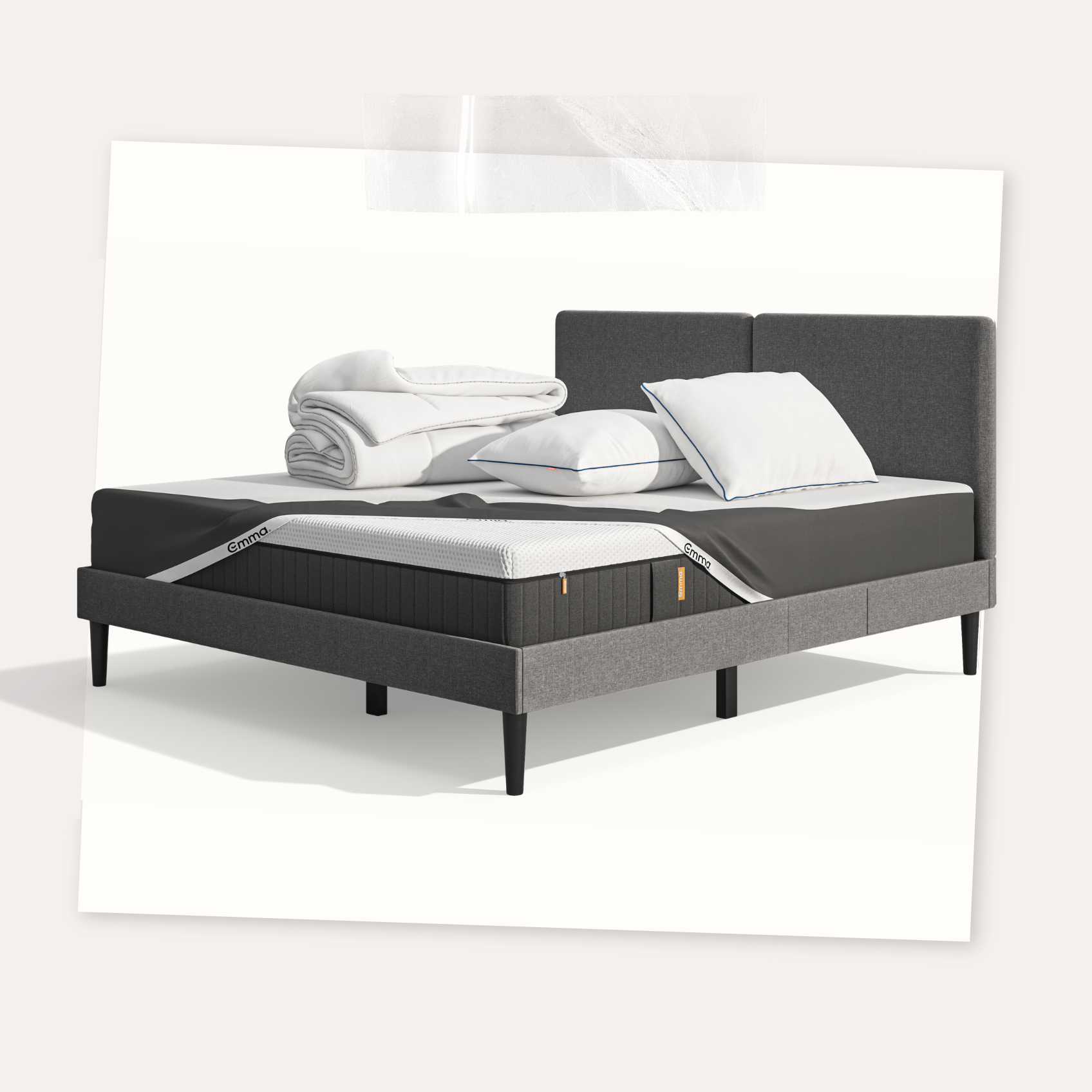 Lit moderne avec tête de lit grise et pieds noirs, recouvert de draps blancs. Deux oreillers blancs et une pile de linge plié sont posés sur le matelas. Arrière-plan beige avec une forme orange abstraite.