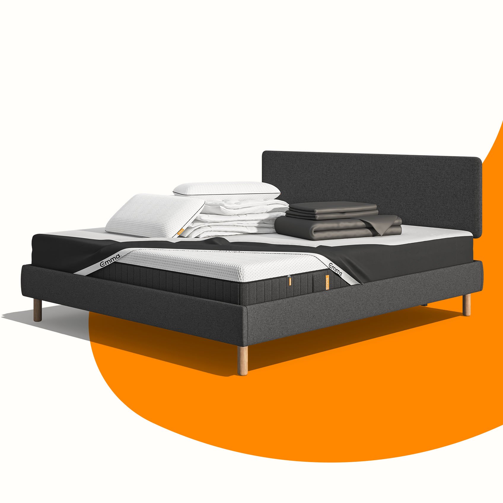 Lit moderne avec tête de lit grise et pieds noirs, recouvert de draps blancs. Deux oreillers blancs et une pile de linge plié sont posés sur le matelas. Arrière-plan beige avec une forme orange abstraite.