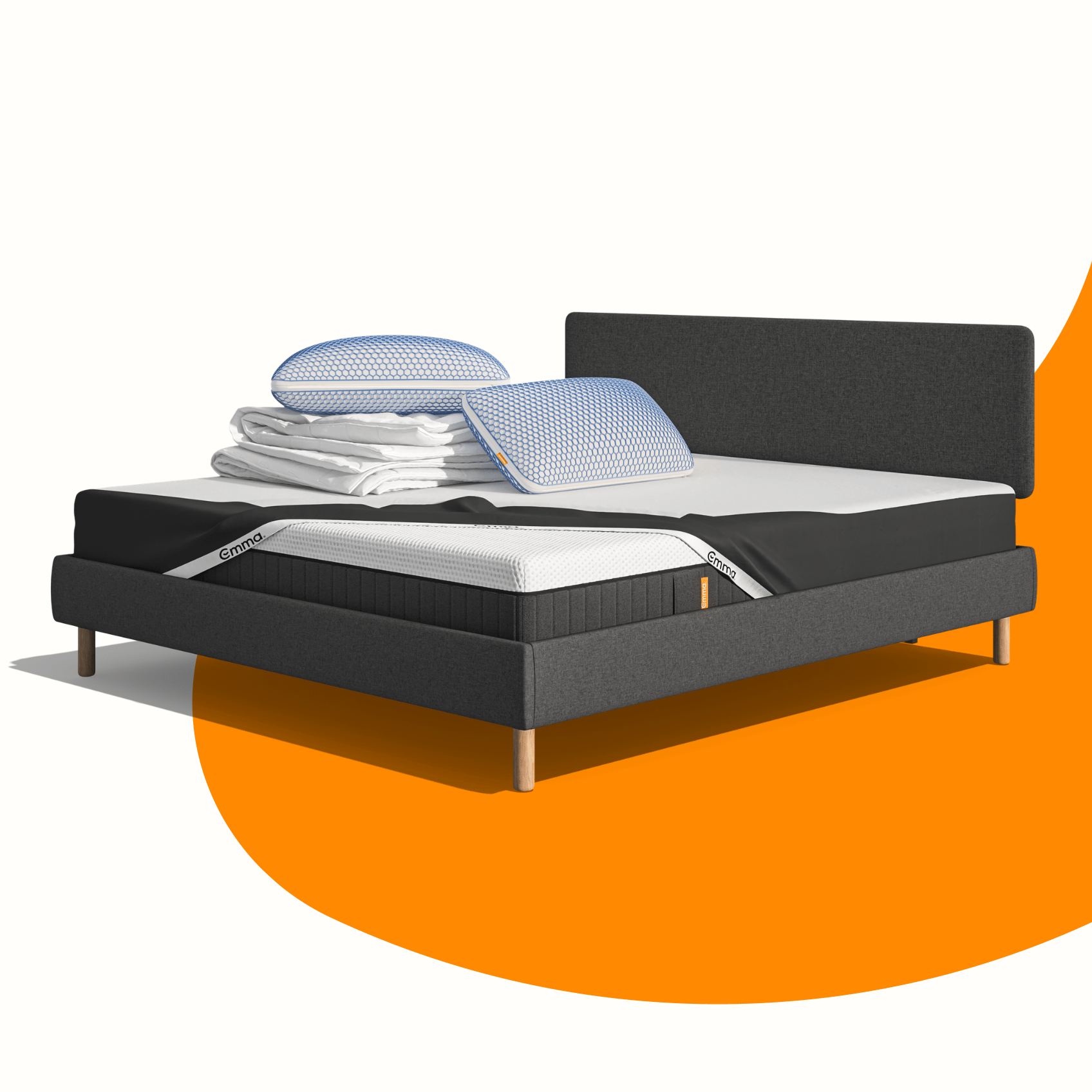 Lit moderne avec tête de lit grise et pieds noirs, recouvert de draps blancs. Deux oreillers blancs et une pile de linge plié sont posés sur le matelas. Arrière-plan beige avec une forme orange abstraite.