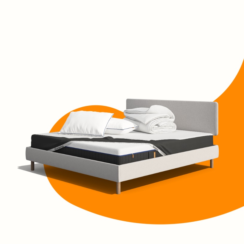 Lit moderne avec tête de lit grise et pieds noirs, recouvert de draps blancs. Deux oreillers blancs et une pile de linge plié sont posés sur le matelas. Arrière-plan beige avec une forme orange abstraite.