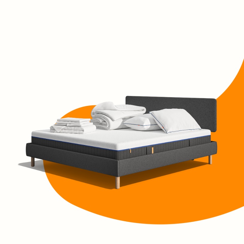 Lit moderne avec tête de lit grise et pieds noirs, recouvert de draps blancs. Deux oreillers blancs et une pile de linge plié sont posés sur le matelas. Arrière-plan beige avec une forme orange abstraite.