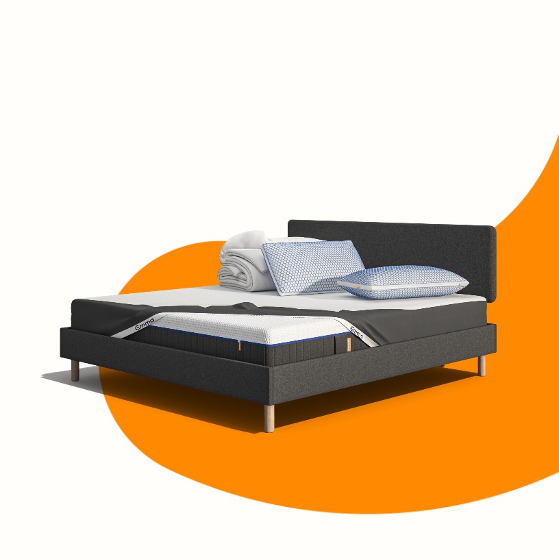 Lit moderne avec tête de lit grise et pieds noirs, recouvert de draps blancs. Deux oreillers blancs et une pile de linge plié sont posés sur le matelas. Arrière-plan beige avec une forme orange abstraite.