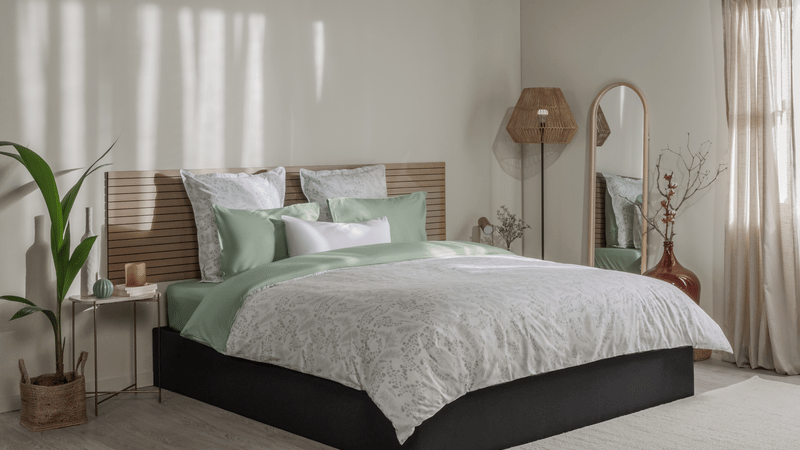 Letto ordinato con biancheria con motivo floreale verde e bianco, testiera in legno e decorazioni su entrambi i lati.