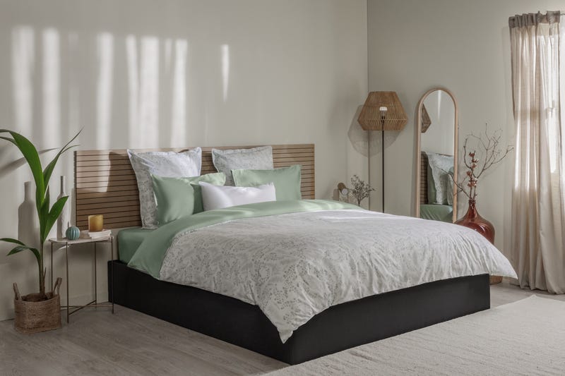 Letto ordinato con biancheria con motivo floreale verde e bianco, testiera in legno e decorazioni su entrambi i lati.