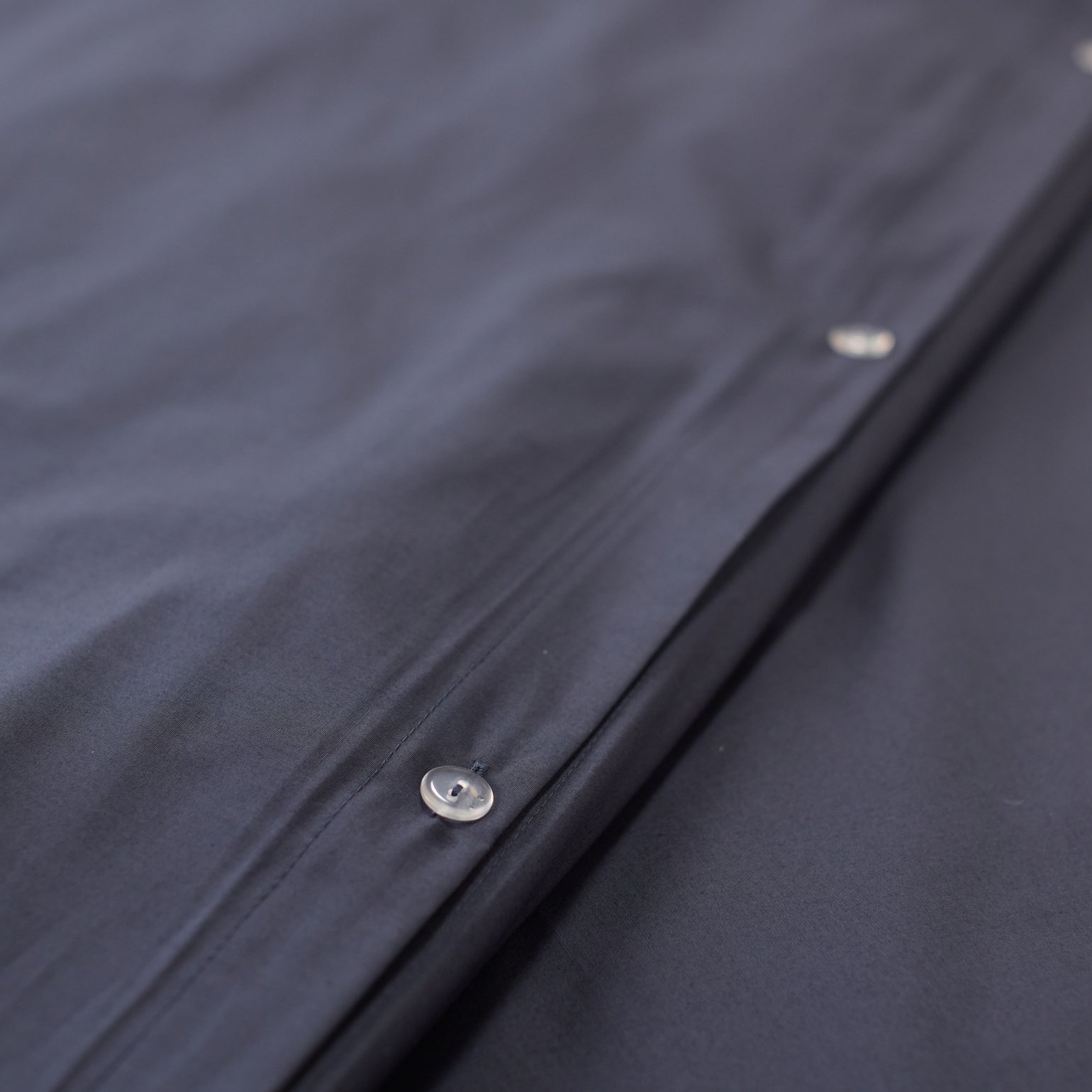 Close‑up van donkergrijs beddengoed met zichtbare knoopsluiting.