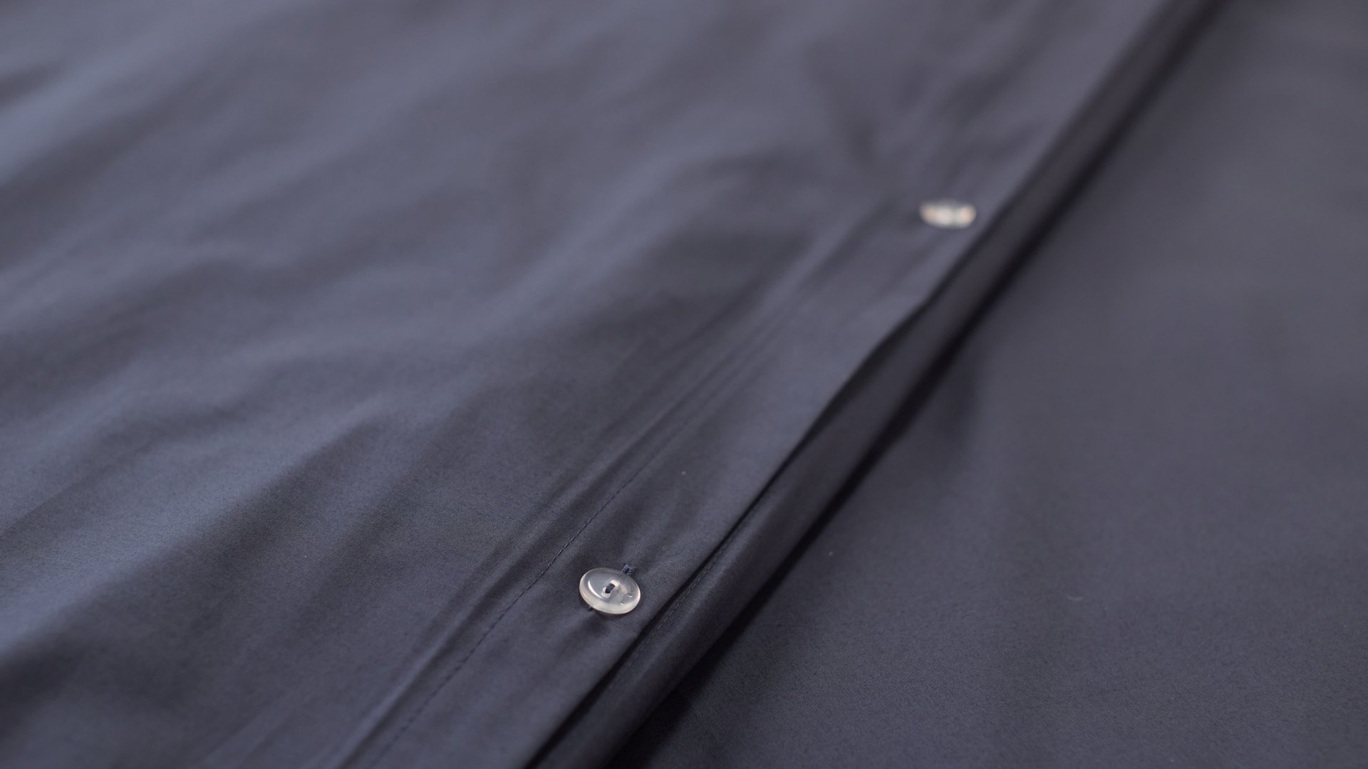 Close‑up van donkergrijs beddengoed met zichtbare knoopsluiting.