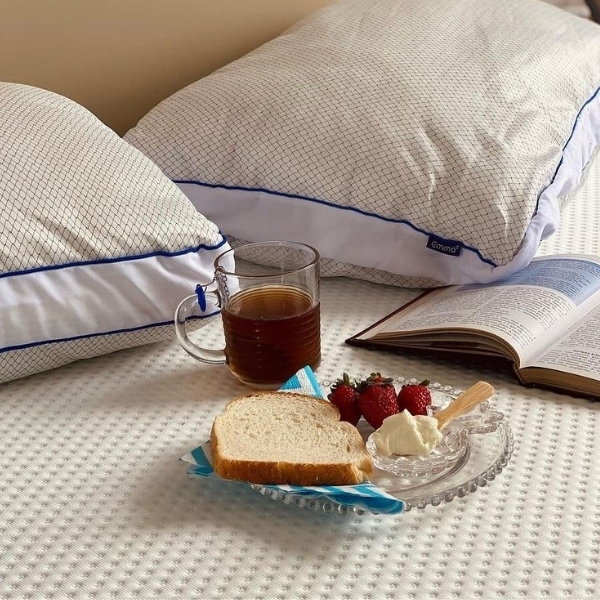 Travesseiros Antiestress Emma em cima de colchão, café da manhã e livro. 