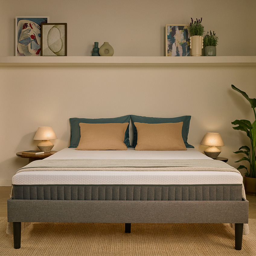 Lit complet avec matelas Emma Hybride, cadre de lit gris et oreillers beiges dans une chambre moderne.