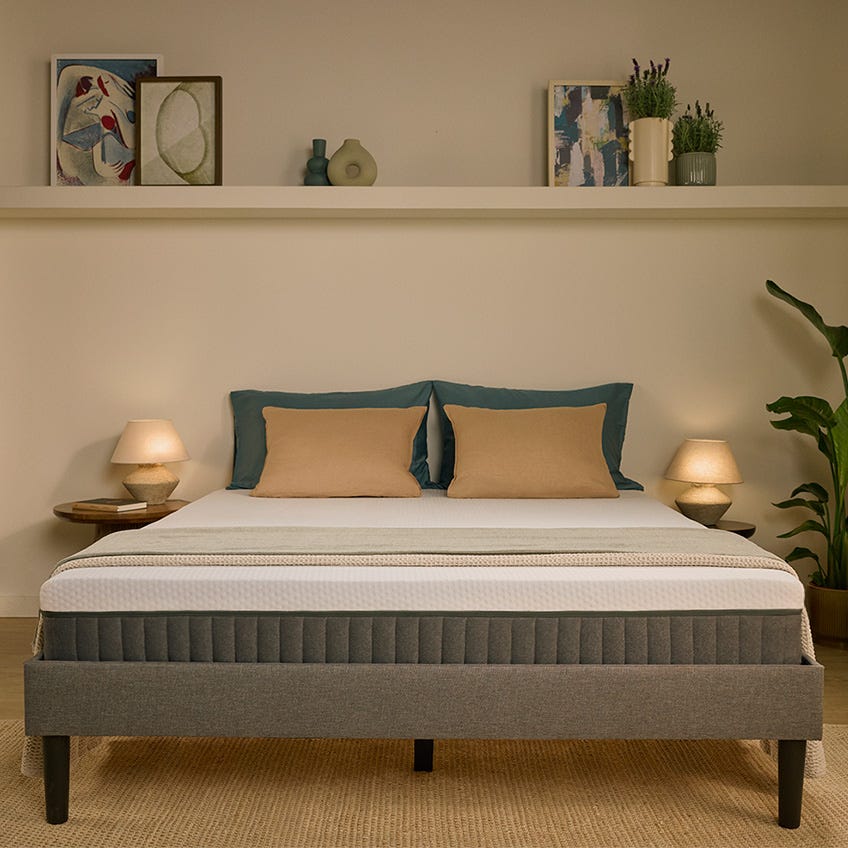 Lit complet avec matelas Emma Hybride, cadre de lit gris et oreillers beiges dans une chambre moderne.