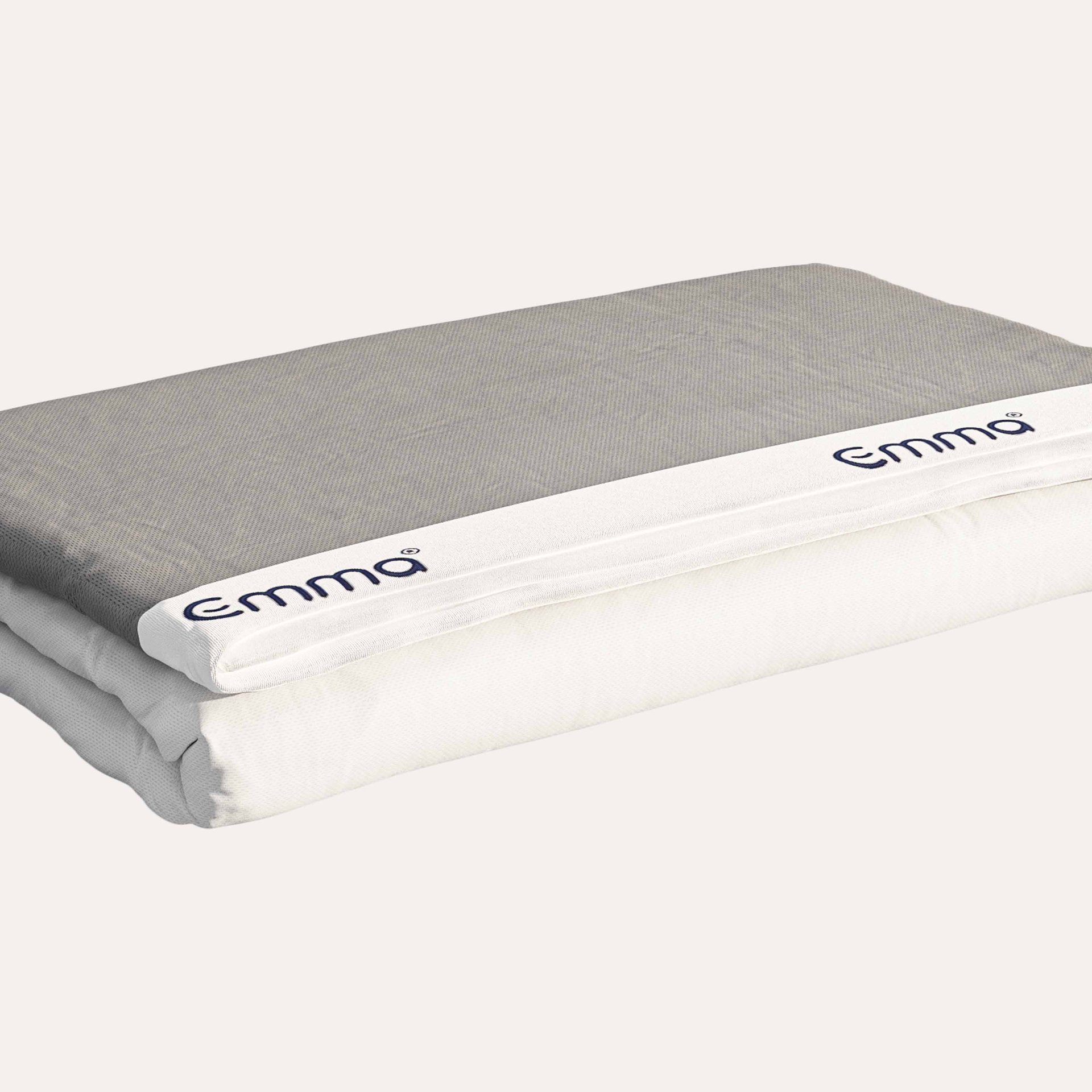 coprimaterasso piegato con strato superiore grigio e bordo bianco con marchio 'Emma'.