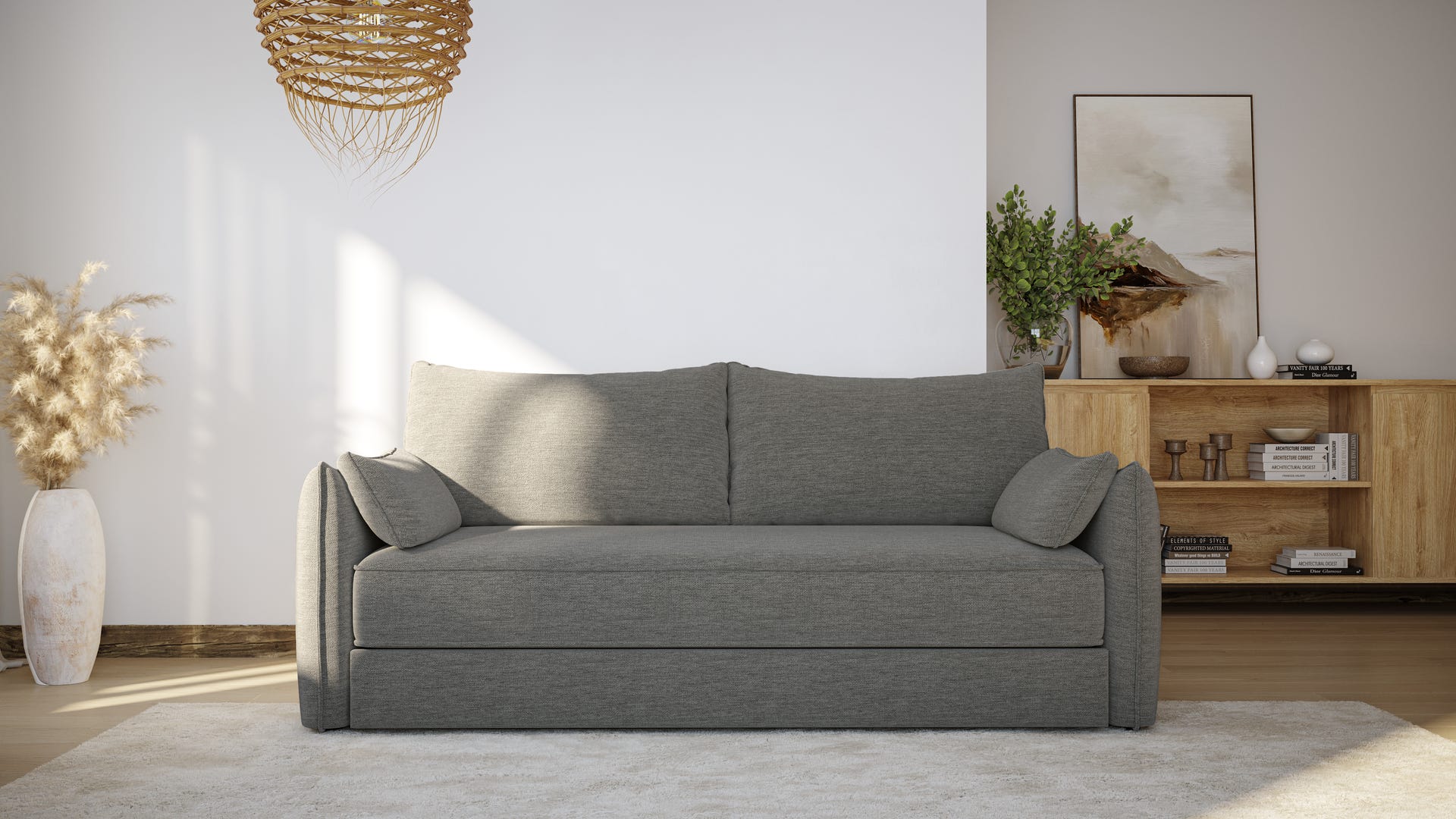 Canapé convertible gris foncé au design minimaliste, avec deux coussins assortis. Placé sur un tapis clair dans un salon lumineux. Mur blanc avec décoration murale tressée à gauche. À droite, buffet en bois avec étagères ouvertes et placards fermés, décoré de cadres, plantes et objets. Vase blanc avec fleurs claires posé au sol à gauche. Ambiance chaleureuse et contemporaine.