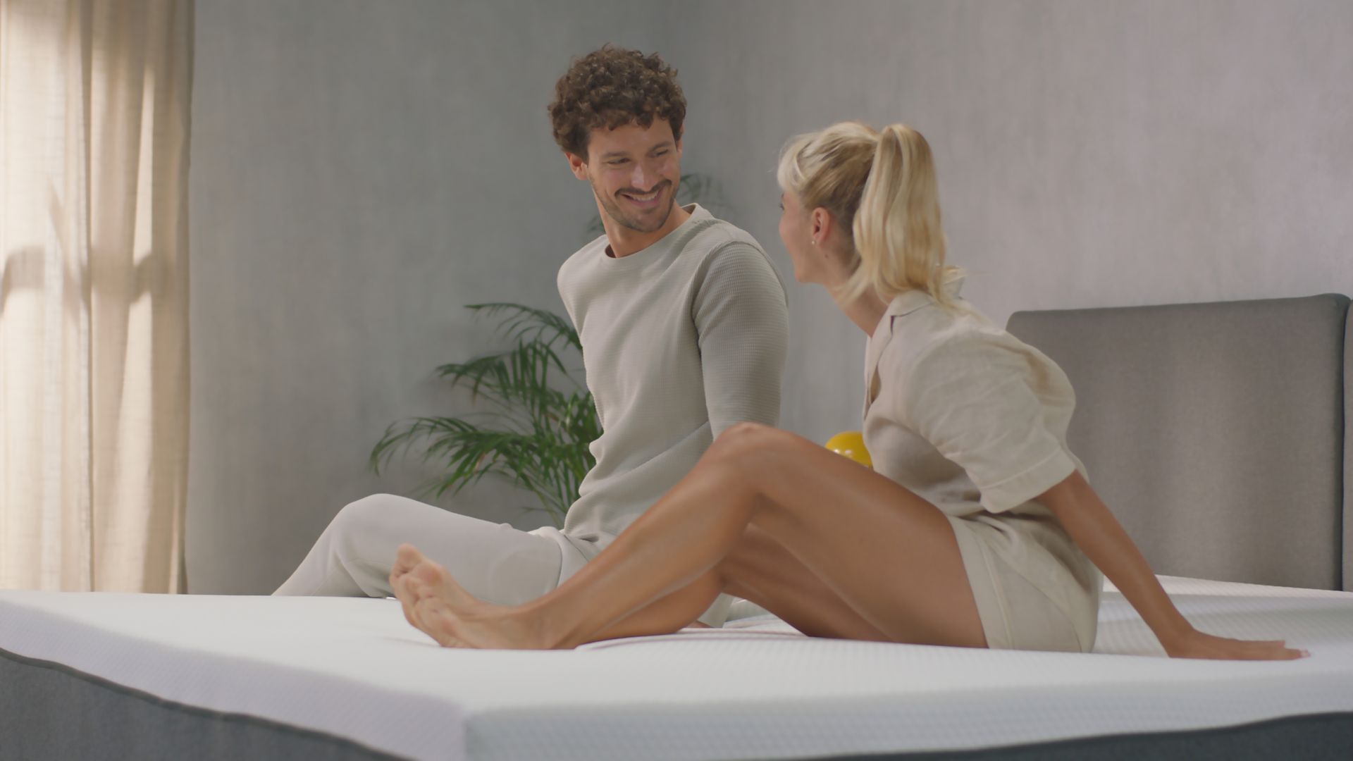 Imagem de um casal feliz e a sorrir, sentados sob um colchão Emma Original