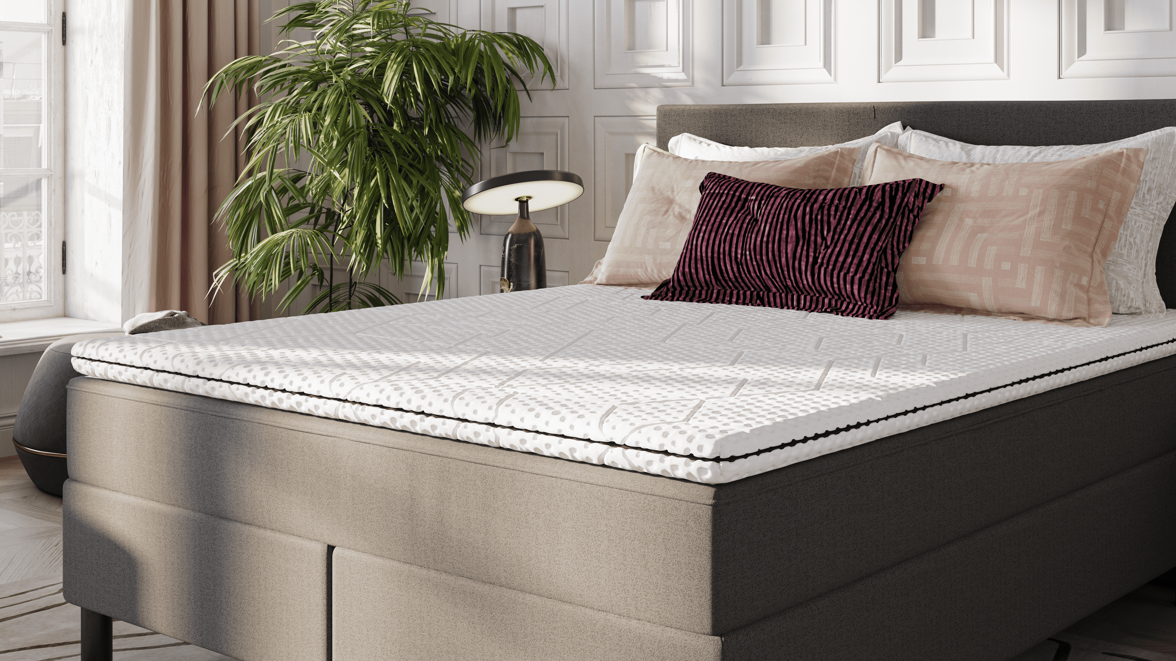 Emma Topper auf Boxspringbett in elegantem Schlafzimmer mit Zierkissen und Tageslicht.