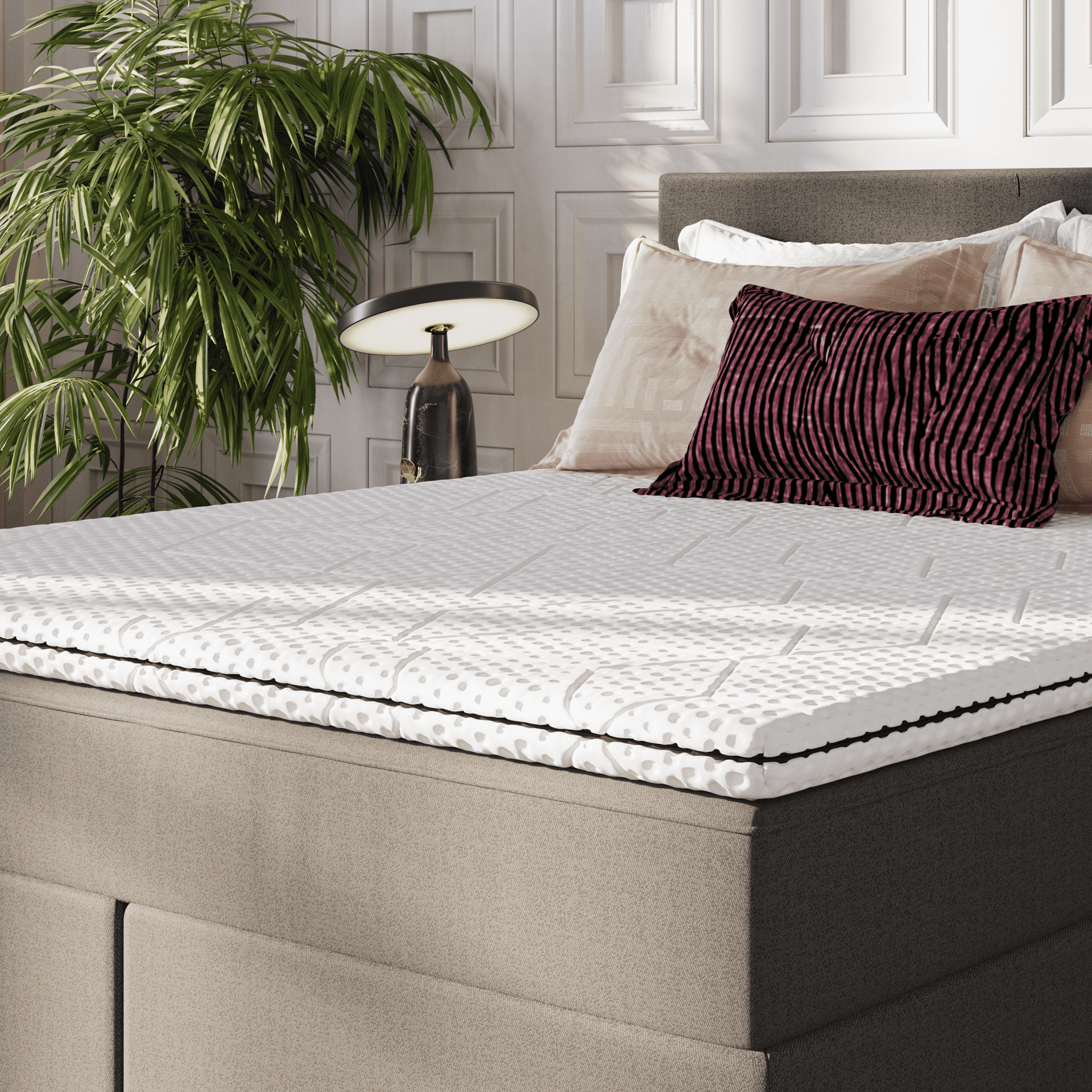 Emma Topper auf Boxspringbett in elegantem Schlafzimmer mit Zierkissen und Tageslicht.