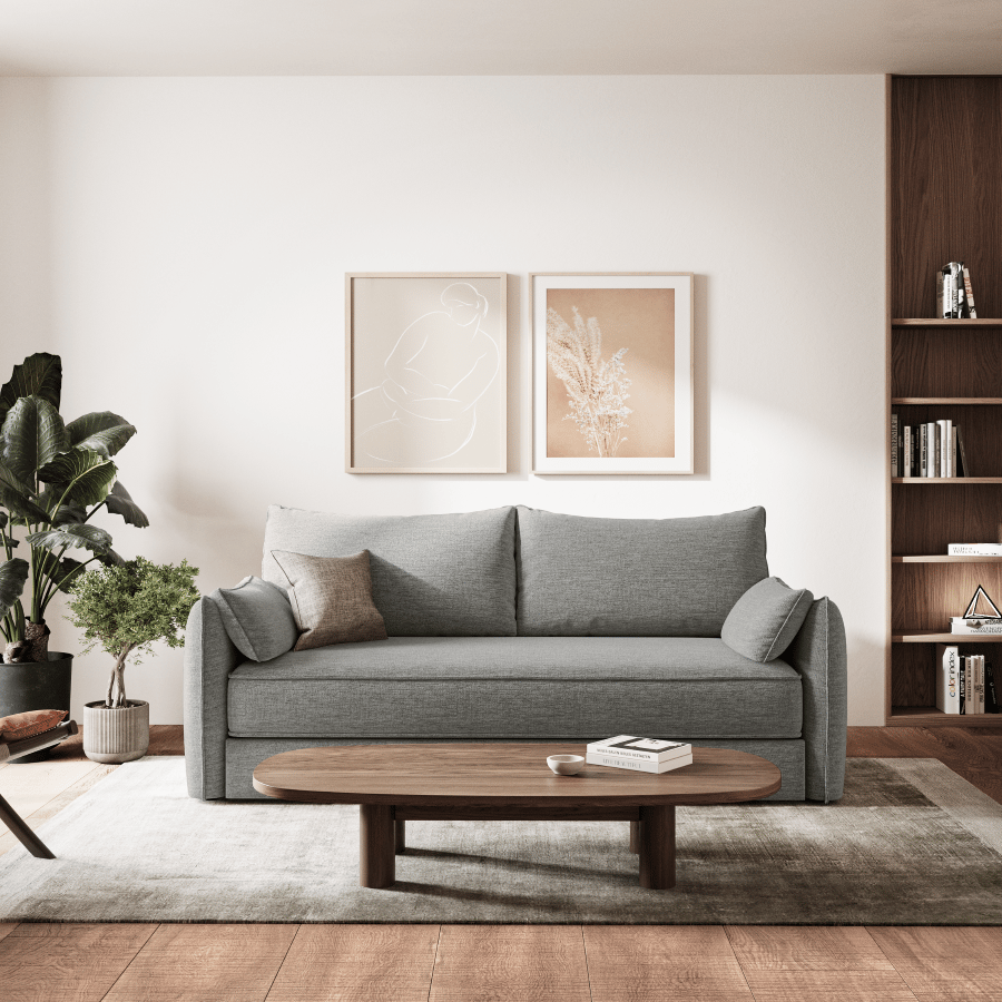 Salon moderne avec canapé gris, table basse en bois, étagère et plantes, comprenant un coin lecture confortable avec un fauteuil marron et une grande fenêtre.