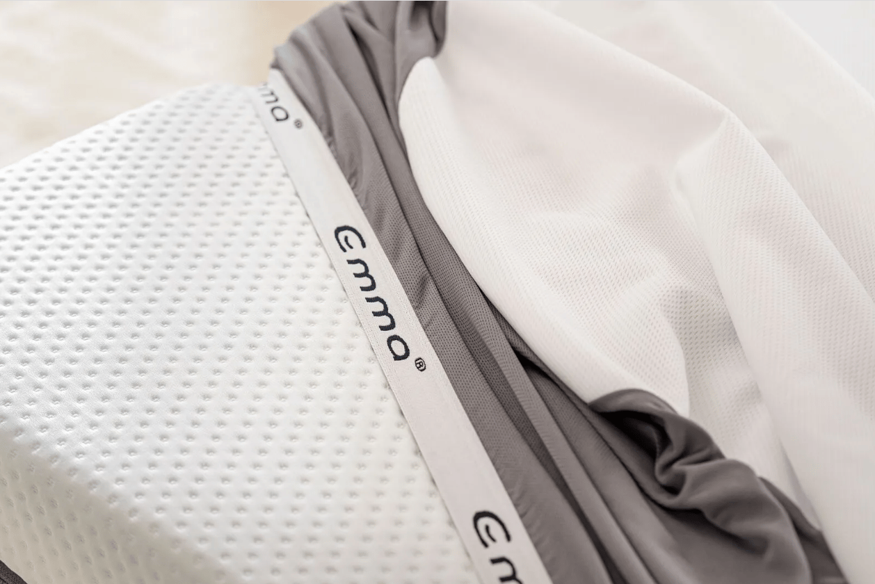 Close-up van de Emma Matrasbeschermer met wit geperforeerd oppervlak, grijze textielrand en zichtbaar Emma-label—ontworpen voor ademend, waterdicht en allergievrij slaapcomfort.